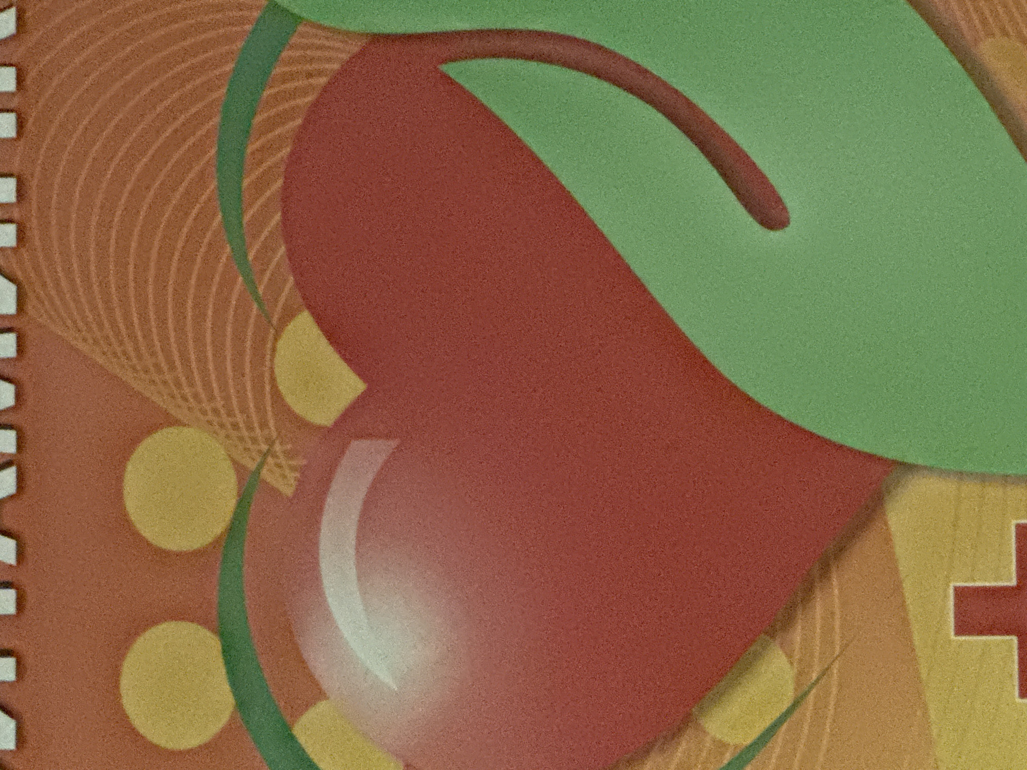 The image displays a close-up of a graphic design. A large red heart, partially encircled by a green curved shape, is the central focus. Behind the heart, there are several yellow circular elements and abstract orange wavy lines. At the bottom left, a red cross symbol is visible. The overall aesthetic is textured and somewhat stylized. The image does not contain any discernible information related to the city of Norilsk, Russia, or any specific geographical or urban setting.