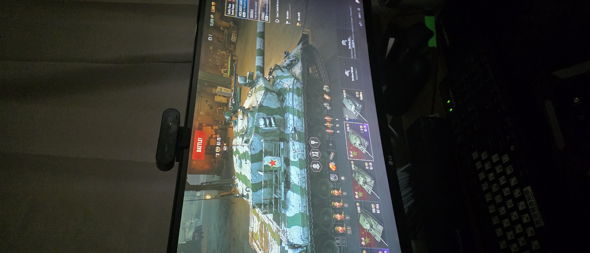 The image shows a computer monitor displaying the game "World of Tanks." The game features a garage view with a tank, identified as the BZ-75, prominently displayed. Various game interface elements are visible, including battle status, vehicle statistics, and in-game currency. The monitor is positioned on a desk, with a keyboard and a computer mouse visible in the foreground. A webcam is mounted on top of the monitor. The environment appears to be a dimly lit room, possibly a home office or gaming setup. The image was captured in Gimhae-si, South Korea.