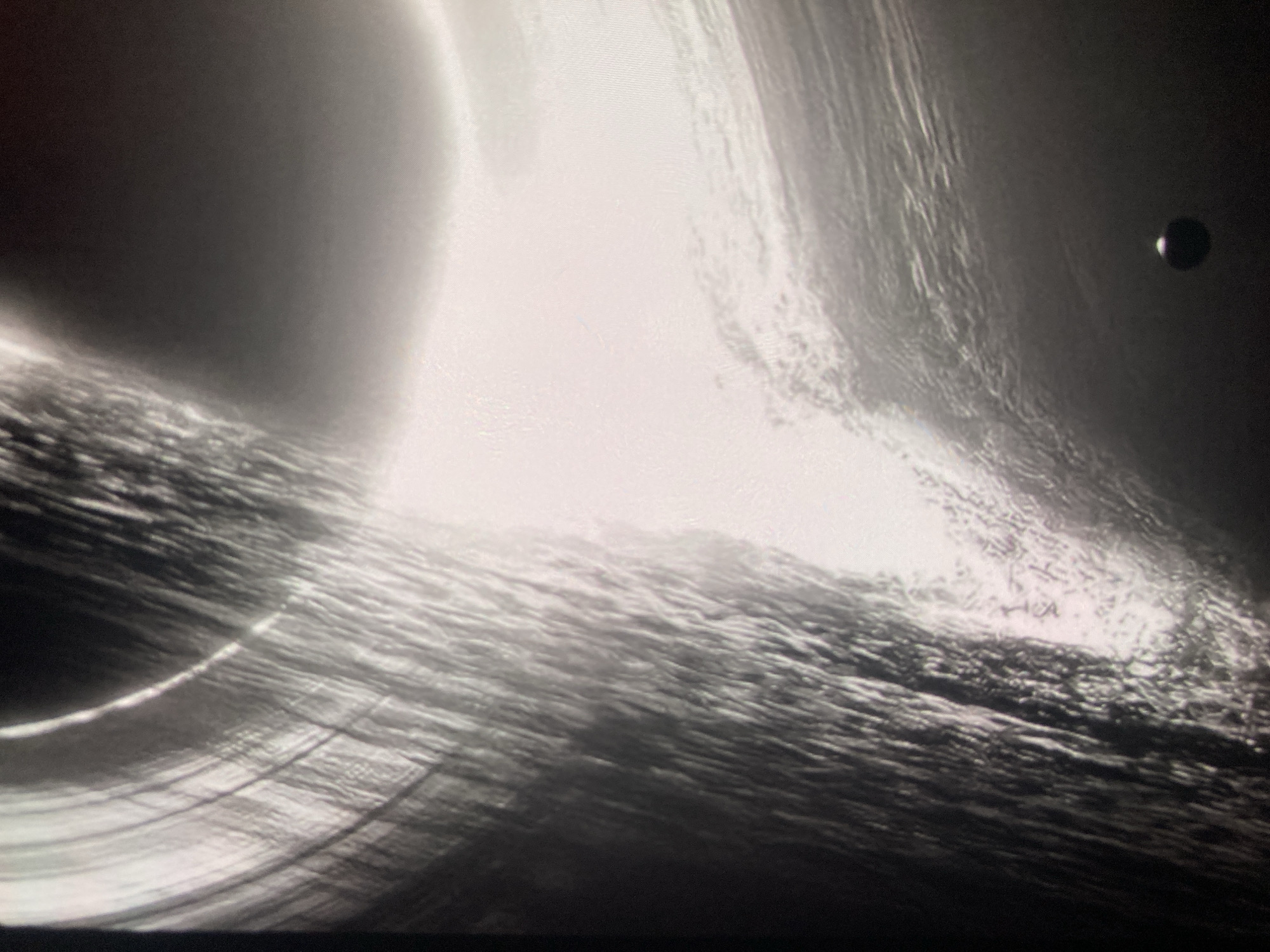 The image is a black and white photograph showing a dark, amorphous shape against a bright, swirling background that suggests a cosmic phenomenon. There are no discernible features of a city or any specific location, therefore, no information can be provided regarding Ustyvytsia, Ukraine. The composition is abstract, with textures that appear to be light and shadow playing across a gravitational anomaly or celestial event. A small, dark circular object with a faint halo is visible in the lower right quadrant.