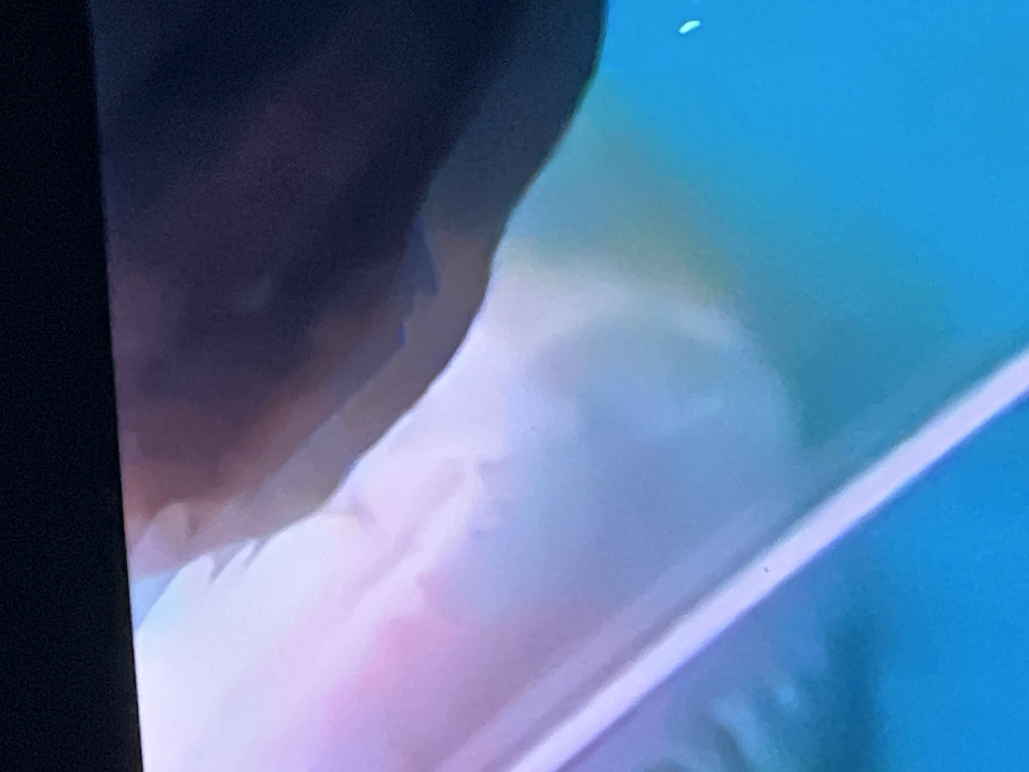 This is a close-up, abstract image with a dark, blurred upper section transitioning into soft, pastel-colored light. The bottom portion of the image is a bright, aqua-blue. There is a faint, thin, diagonal white line across the lower part of the image, with a small dark speck on it. The image does not contain any identifiable elements of the city of Casablanca, Morocco, or any people, subjects, or discernible actions. It appears to be a photograph of light or color patterns.