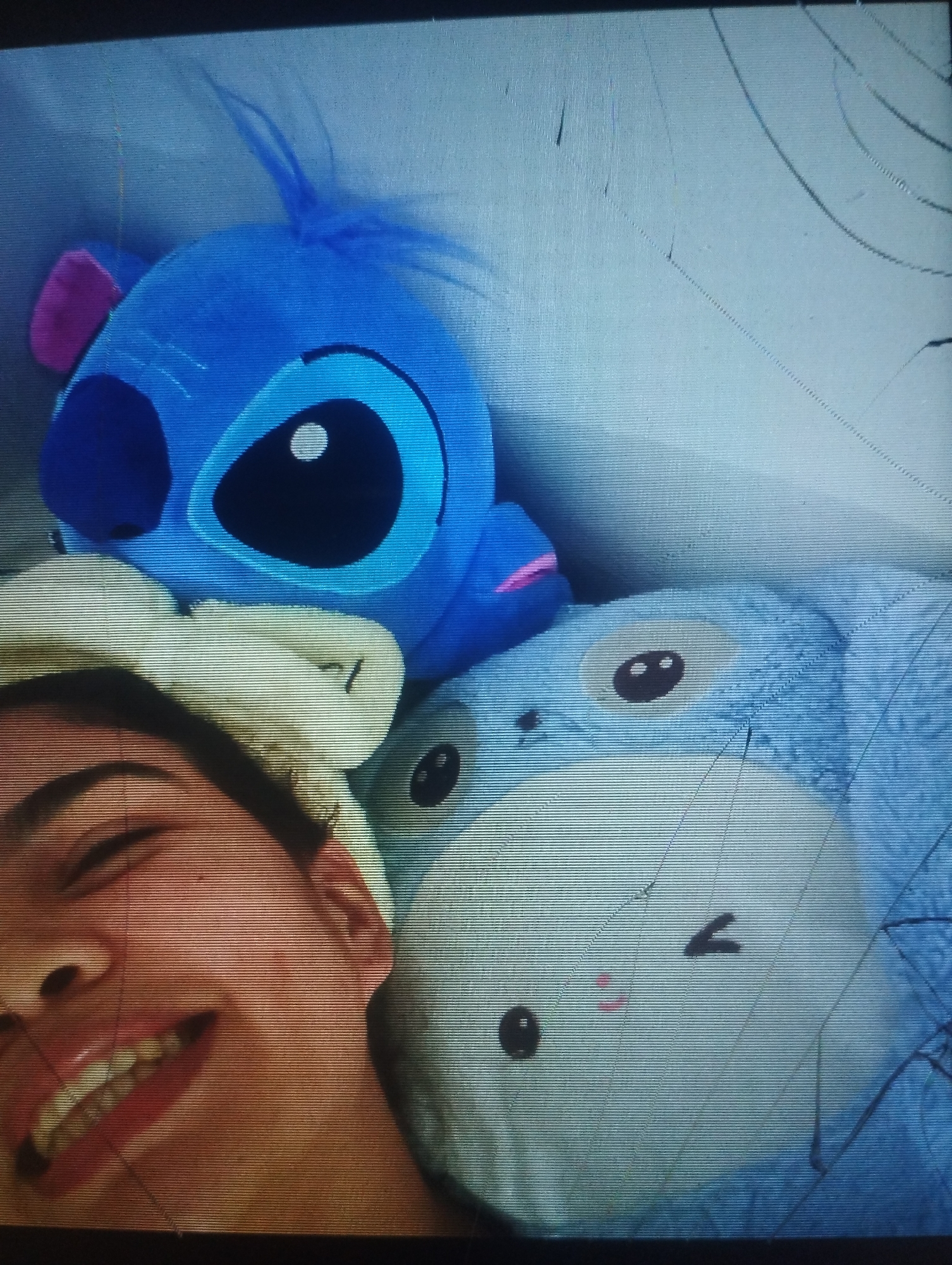 A selfie depicts a smiling person with a white headband, positioned to the left of the frame. Behind the person are three plush toys. The top toy is a blue Stitch character. Below Stitch are two blue bunny-like plush toys, stacked on top of one another. The background appears to be a plain wall or bedding. The photo has damage or cracks. The location, Punta de Piedras, Venezuela, is not visually evident in the image.