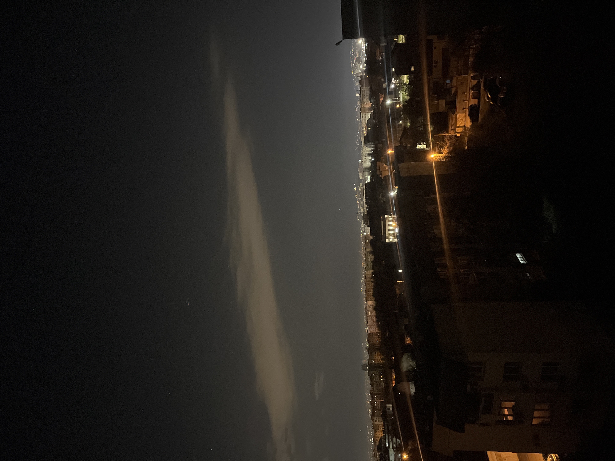 The image shows a nighttime view over a city. On the left is a dark, indistinct area, possibly water or a dark plain with clouds. In the center, a line of city lights stretches into the distance. On the right, buildings and streets are visible, illuminated by streetlights.
Without additional context, pinpointing the precise location in Sofia, Bulgaria, is difficult. Further, the image shows very few people, objects or actions, so those are not described.