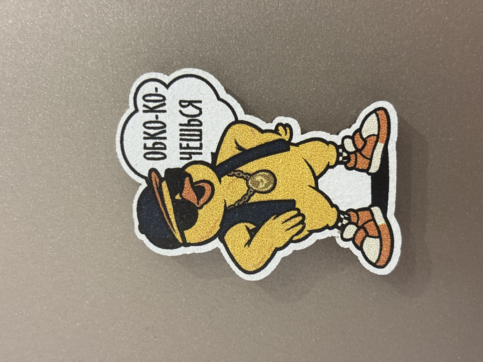 The image shows a sticker of a cartoon duck wearing sunglasses, a hat, a chain, and sneakers. The duck is lying on its back. A speech bubble next to the duck contains text in Russian: "Очко-ко-чешься." The sticker is placed on a grey, possibly metallic, surface. There is no indication of Zagatuy, Russia.