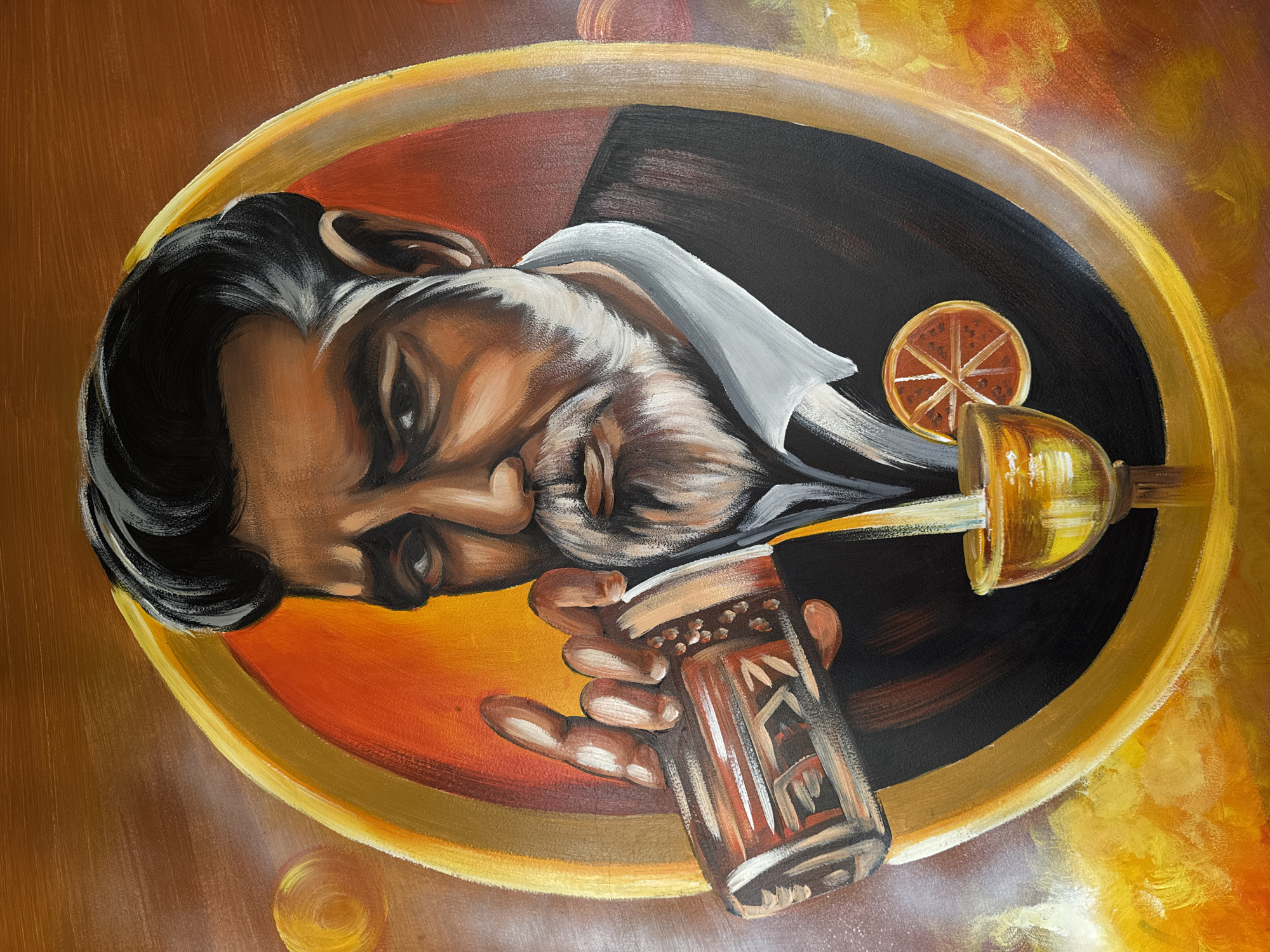 A painting depicts a man in a dark suit with a white shirt, holding a glass with brown liquid, possibly liquor. The glass is decorated with geometric patterns. The man's face is rendered with a somewhat somber expression. A circular slice of citrus fruit sits beside him. A gold-colored goblet pours liquid into the glass. The image is framed by an oval with golden and brown concentric bands. The background has an abstract, painterly texture in shades of gold and brown. The scene's location in Đà Nẵng, Vietnam, is not evident from the image.
