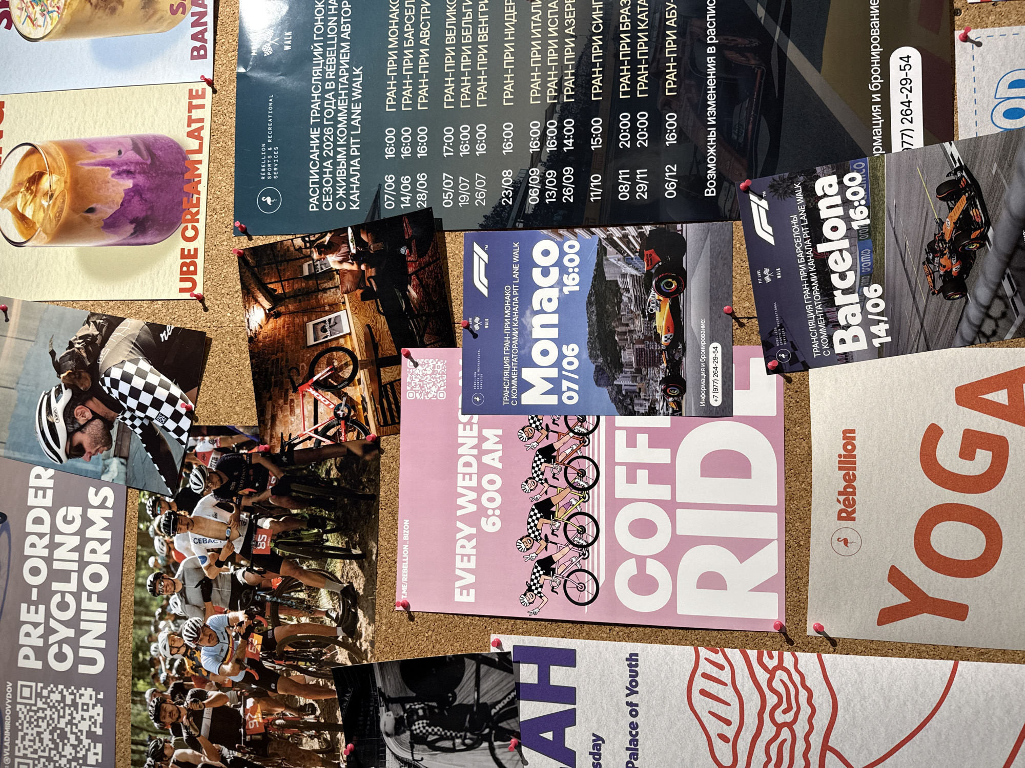 This media file contains a collage of several images pinned to a corkboard. The primary subjects are cyclists and promotional materials for cycling events and related merchandise.
One prominent image features a group of cyclists in full gear, appearing to be in a race or group ride, with the text "PRE-ORDER CYCLING UNIFORMS" visible on a separate poster. Another image shows a close-up of a latte with purple and brown swirls.
Several posters advertise live broadcasts of Formula 1 races, listing event names like "Monaco," "Barcelona," and various Grand Prix races with dates and times in June, August, September, October, November, and December of 2026. Some of these posters also include contact information for "Rebellion" and mention live commentary from the "PIT LANE WALK" channel. One poster highlights "EVERY WEDNES 6:00 AM" with an illustration of cyclists. Another poster displays the word "YOGA" in large, orange lettering next to the "Rebellion" logo.
The overall setting appears to be an indoor space, possibly an office or a community gathering point, where these images and posters are displayed. The corkboard suggests a pinned collection of various announcements and imagery. The visible text is predominantly in Russian, with some English phrases. The emotions conveyed are likely related to enthusiasm for cycling and motorsports.