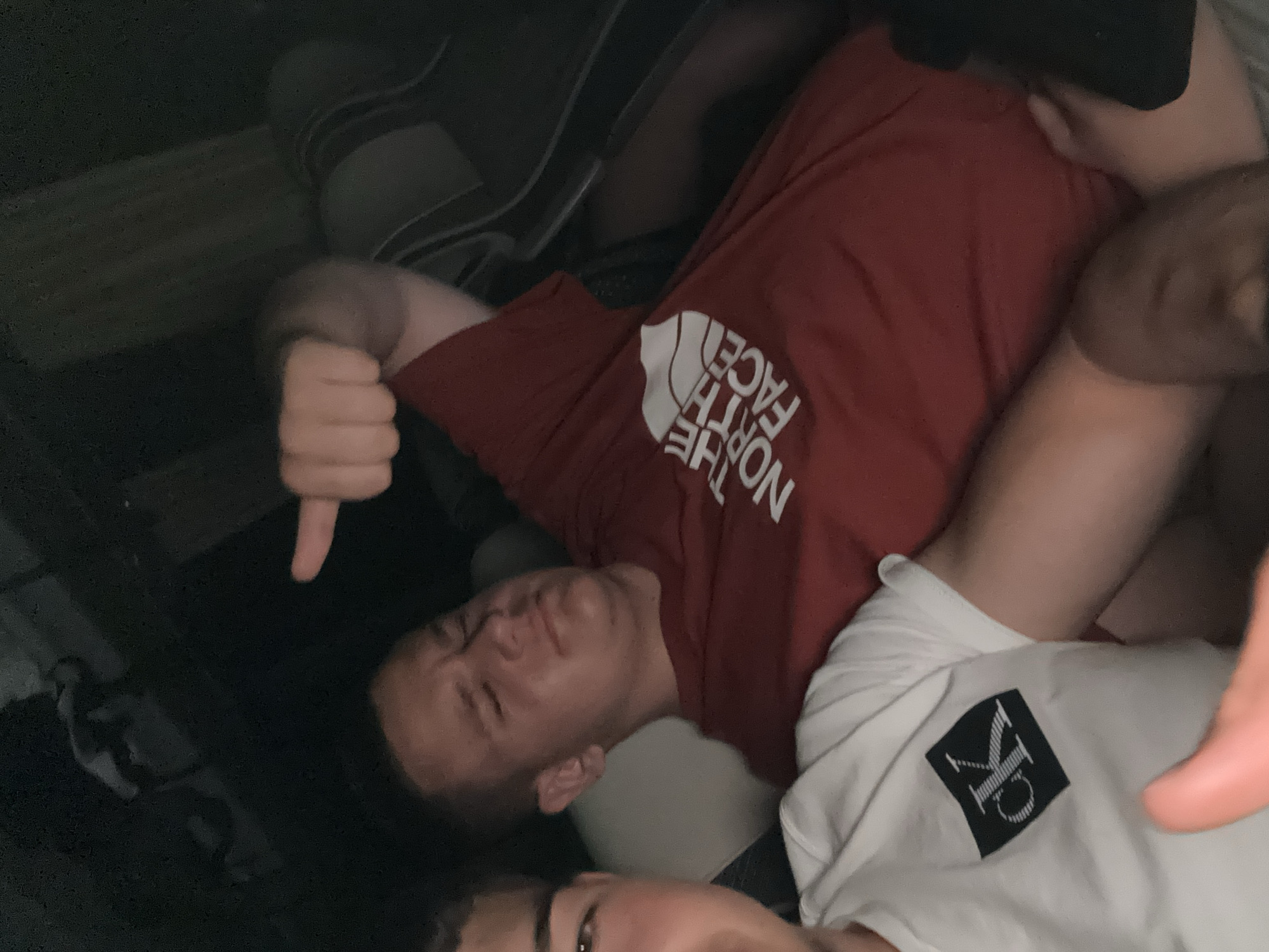 Three people are crammed in a dark, tight space. One person, wearing a red t-shirt with "THE NORTH FACE" printed on it, is making a thumbs down gesture. Another person is wearing a white t-shirt with "CK" printed on it. The location is unknown, as the image does not provide any visual indicators of Bogdanitsa, Bulgaria.