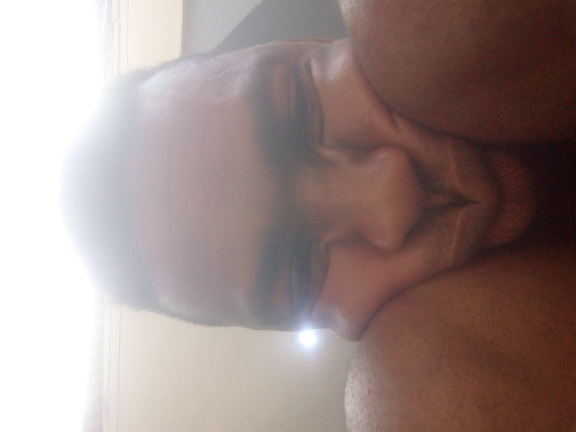 A close-up, blurry, indoor shot features a man's face and part of his upper body, seemingly resting on his shoulder. The man has dark hair, and closed eyes. The background is a light-colored wall. The lighting is harsh, especially on the left side of the frame, creating a strong glare. There is no information in the image to indicate the location is in Ikorodu, Nigeria.