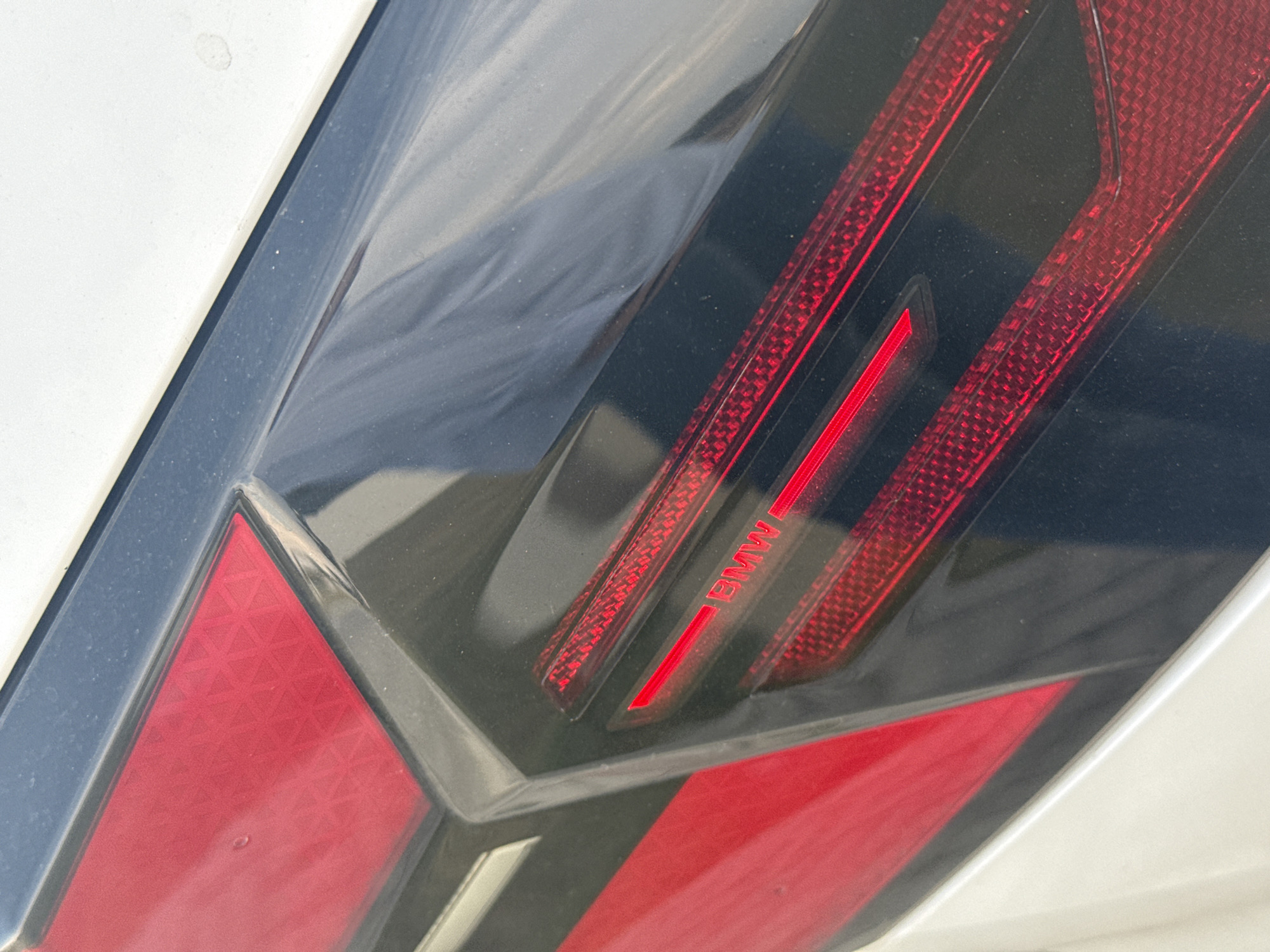 The image shows a close-up of a BMW tail light. The light is red and black, with a small "BMW" label. The vehicle appears to be white. The scene does not provide information about the location or environment to determine its location in San Bernardino Tlaxcalancingo, Mexico.