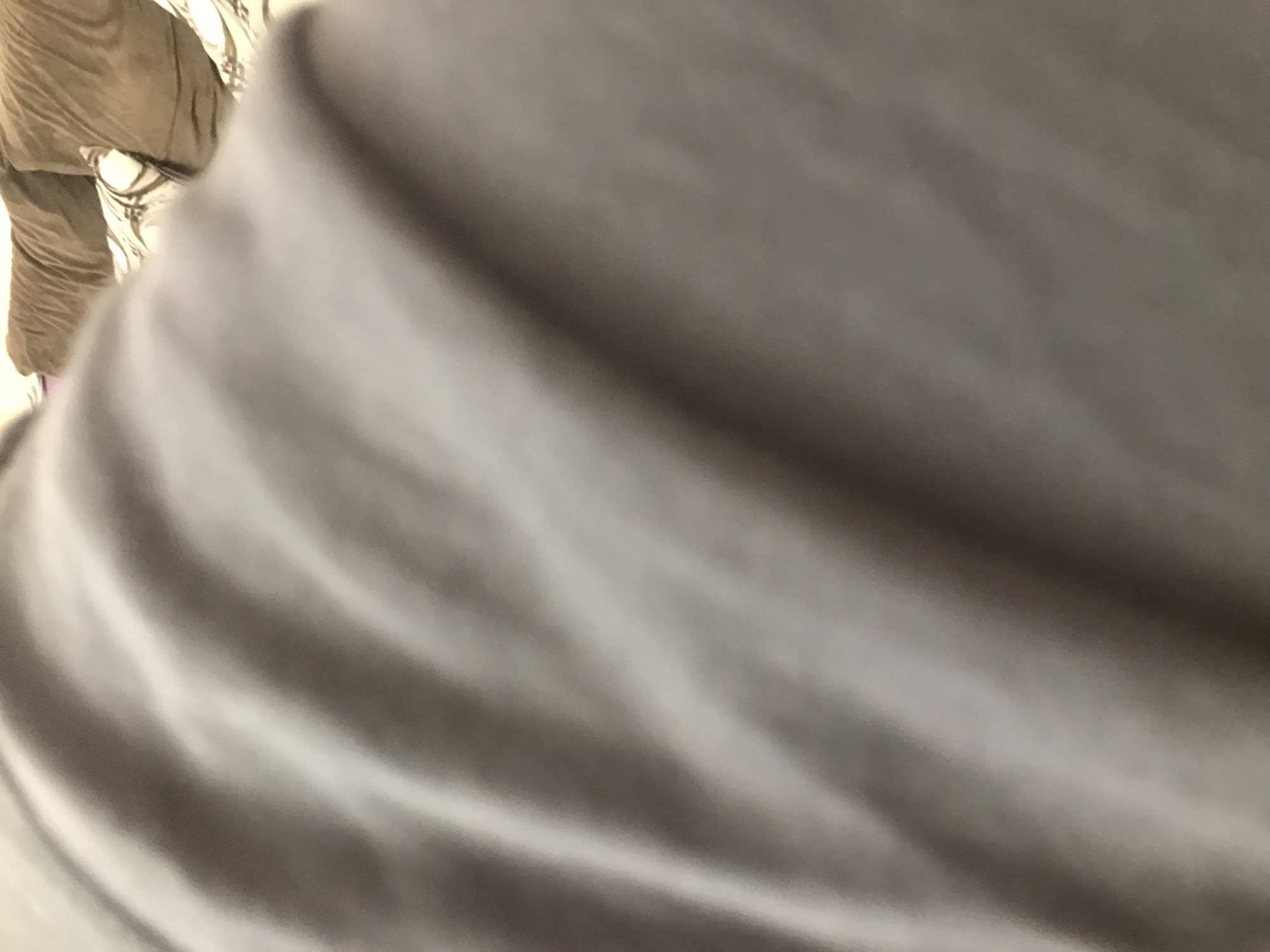The image shows a close-up of a gray, wrinkled surface, possibly fabric, with blurred objects in the background. There is a piece of clothing in the upper left corner that is beige or light brown with stitched seams. The overall scene does not provide enough information to determine a specific location in Yerevan, Armenia, or any other details about people, actions, or the environment.