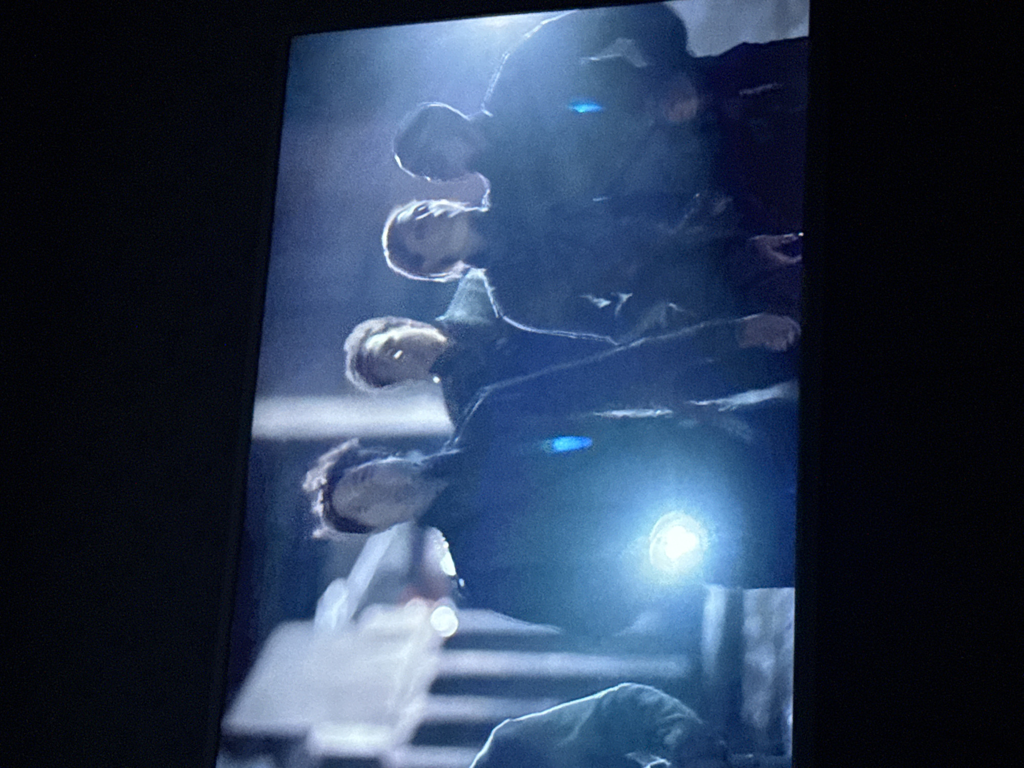 The image depicts four people standing on what appears to be a staircase in an urban setting. The lighting is dim, with a bright light source obscuring details but illuminating the lower part of the scene. The staircase is made of concrete or a similar material, and there are vertical bars that may be part of a railing. No identifying elements indicate that the location is Mytishchi, Russia.