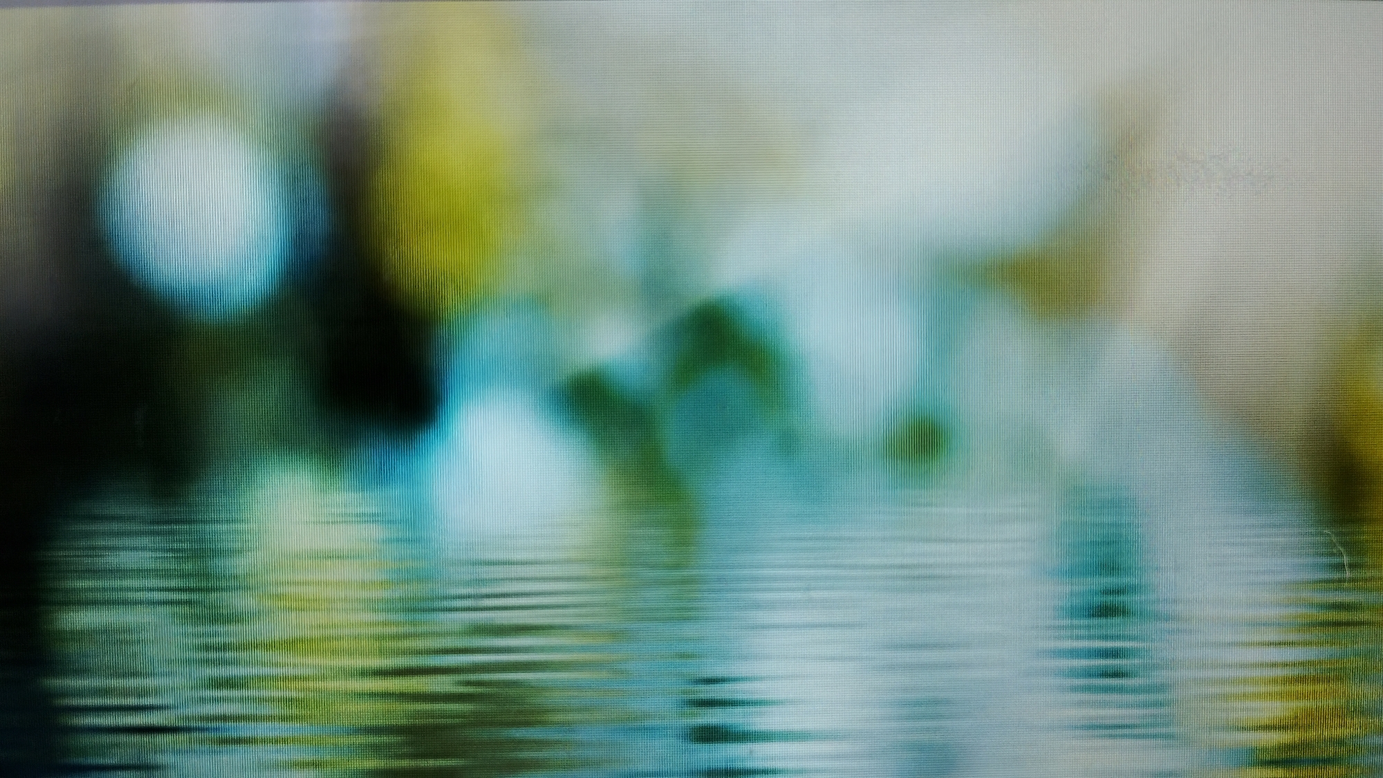 The image is an abstract, out-of-focus photograph with a distinctive horizontal line pattern, suggesting it might be a digital display with some visual artifact or a textured surface. The upper portion of the image features blurry shapes in shades of green, blue, and white, possibly representing foliage or light reflections. The lower portion of the image depicts a wavy, reflective surface with horizontal lines, mimicking water. There are no discernible people, subjects, or specific objects. The scene is entirely abstract and does not provide any identifiable information about a location in Smolyan, Bulgaria, or any other specific place.
