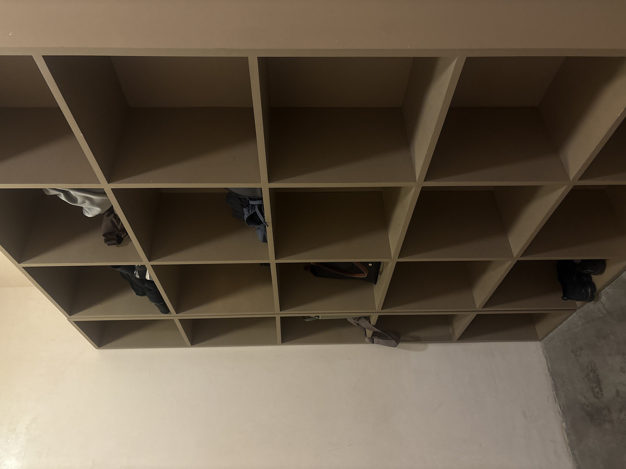 A low-angle shot depicts a light brown shelf with 20 cubbies; some cubbies contain various items of clothing and accessories. The walls are light-colored, and the floor on the right side of the frame appears to be concrete. The location is within Mexico City, Mexico.