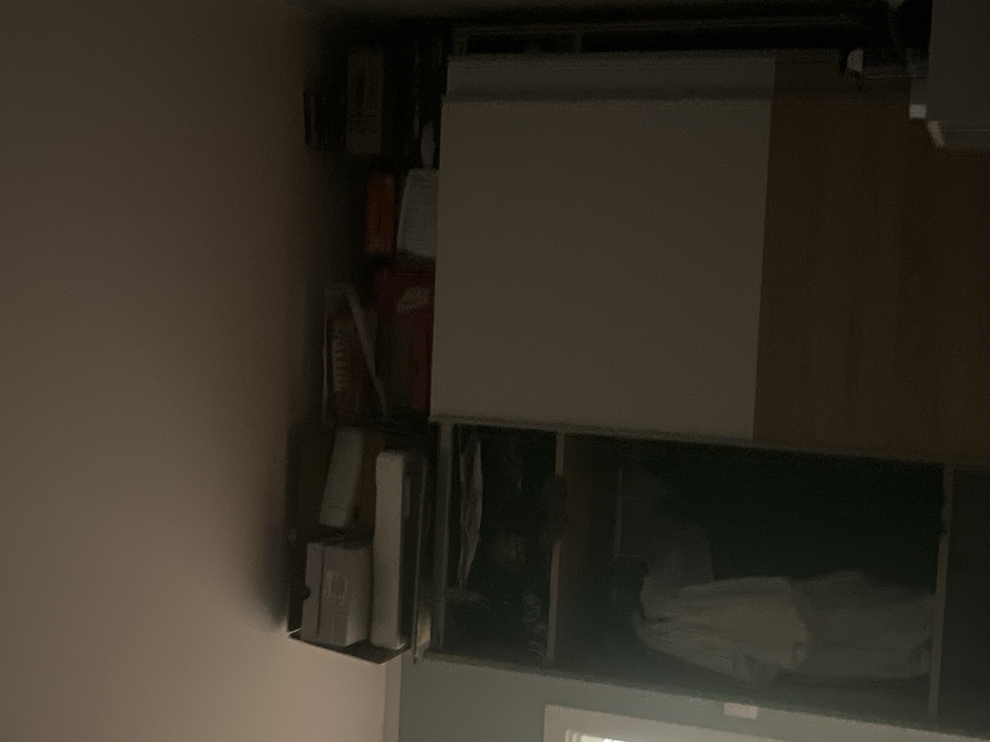 I lack the ability to determine the location of this image, including whether it is in Pokrovnik, Bulgaria. The image shows a partially open kitchen cabinet. The top section of the cabinet contains boxes and containers, with some items visible. The bottom section is darker, but contains what appears to be a white, soft object. A window can be seen partially obscured by the open cabinet door.