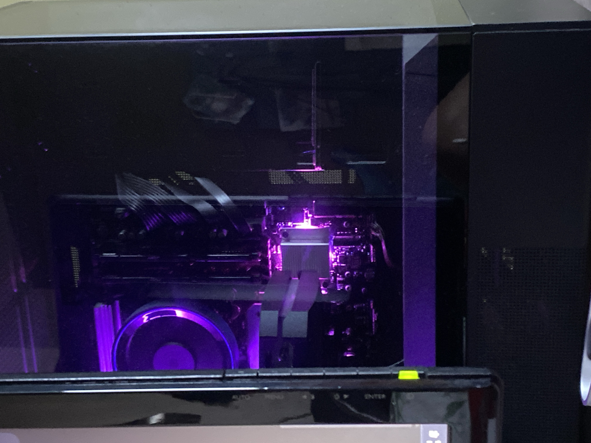 A view of the interior of a computer case, illuminated with purple LED lighting, is partially obscured by a monitor in the foreground. Inside the case, components like the graphics card and cooling fan are visible. The computer case is situated indoors and cannot be located in Sofia, Bulgaria with available information.