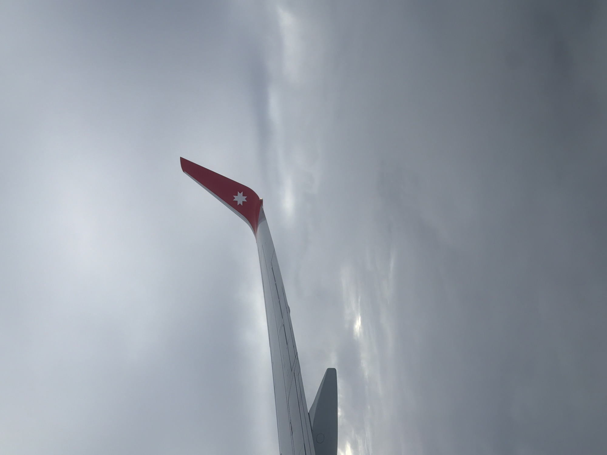 An airplane wing, with a red tip featuring a white star logo, extends from the left side of the frame, cutting diagonally across the image. The wing is white with visible panel lines. The background is a uniform expanse of overcast sky, with variations in grey tones indicating clouds. There is no discernible city, landscape, or people visible. The image appears to be taken from inside an aircraft, looking out at the wing and sky. The specific location in Dubrovo (Uleiminskoe S/P), Russia, cannot be determined from the visual information provided.
