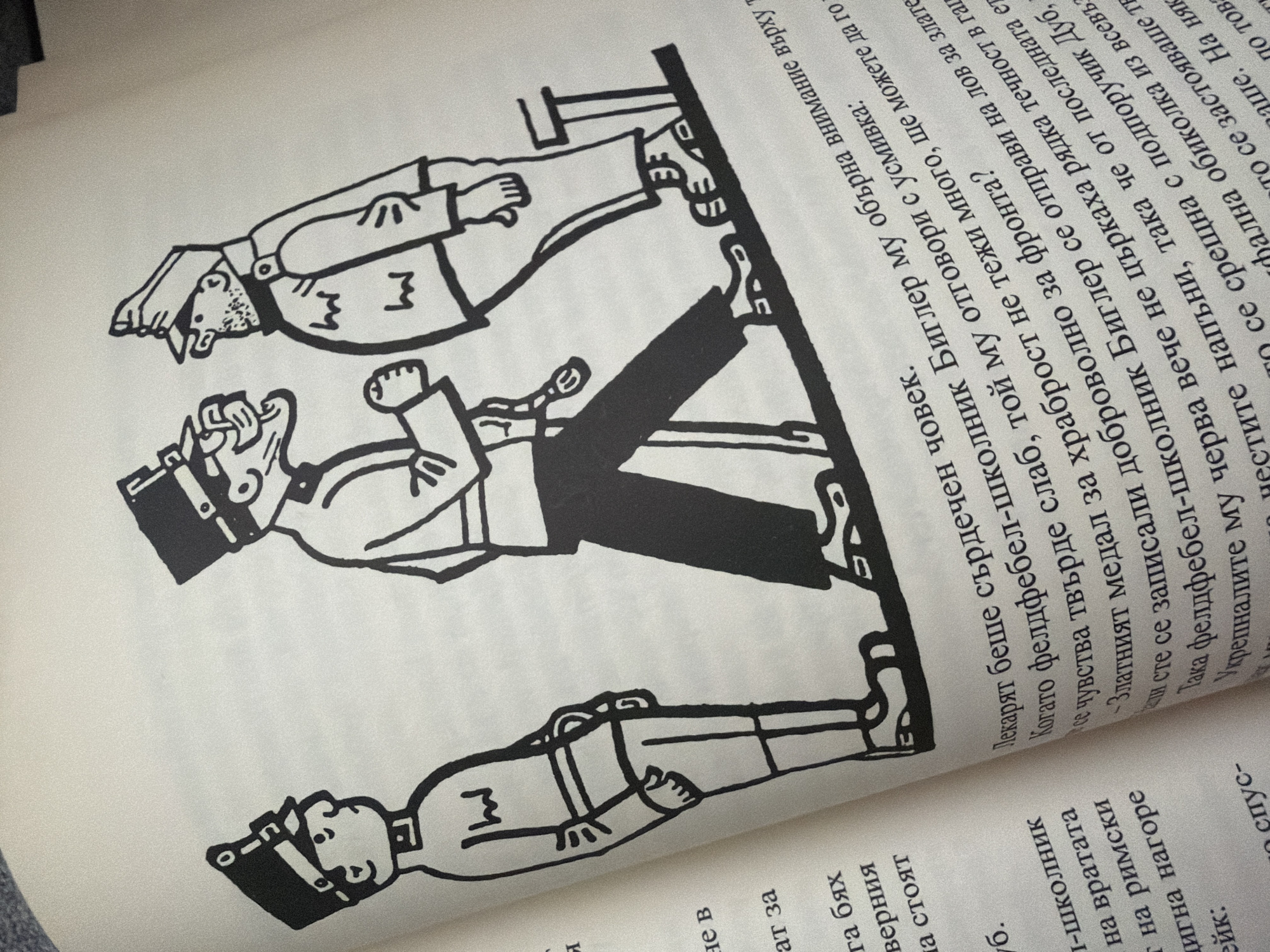 The image is a black and white illustration from a book depicting three figures in military-style uniforms. The figures are drawn in a cartoonish, exaggerated style.
The figure on the left is a young boy wearing a cap with a brim and a medal. He stands with his hands at his sides, looking to the right.
The figure in the center is a taller man with a stern expression, wearing a cap and a uniform with a visible medal or insignia. He is depicted mid-stride, walking to the right, with his left arm bent and his right hand slightly raised, holding what appears to be a lanyard or strap.
The figure on the right is another man, also in uniform and wearing a cap. He is shown facing the central figure and speaking to him, with his hands gesturing.
All three figures are standing on a diagonal line, suggesting they are on a slope or a ramp. The background is plain white, indicating this is an illustration within a book or document.
There is no visible indication of the city of Pazardzhik, Bulgaria, in this image. The image content is solely illustrative.