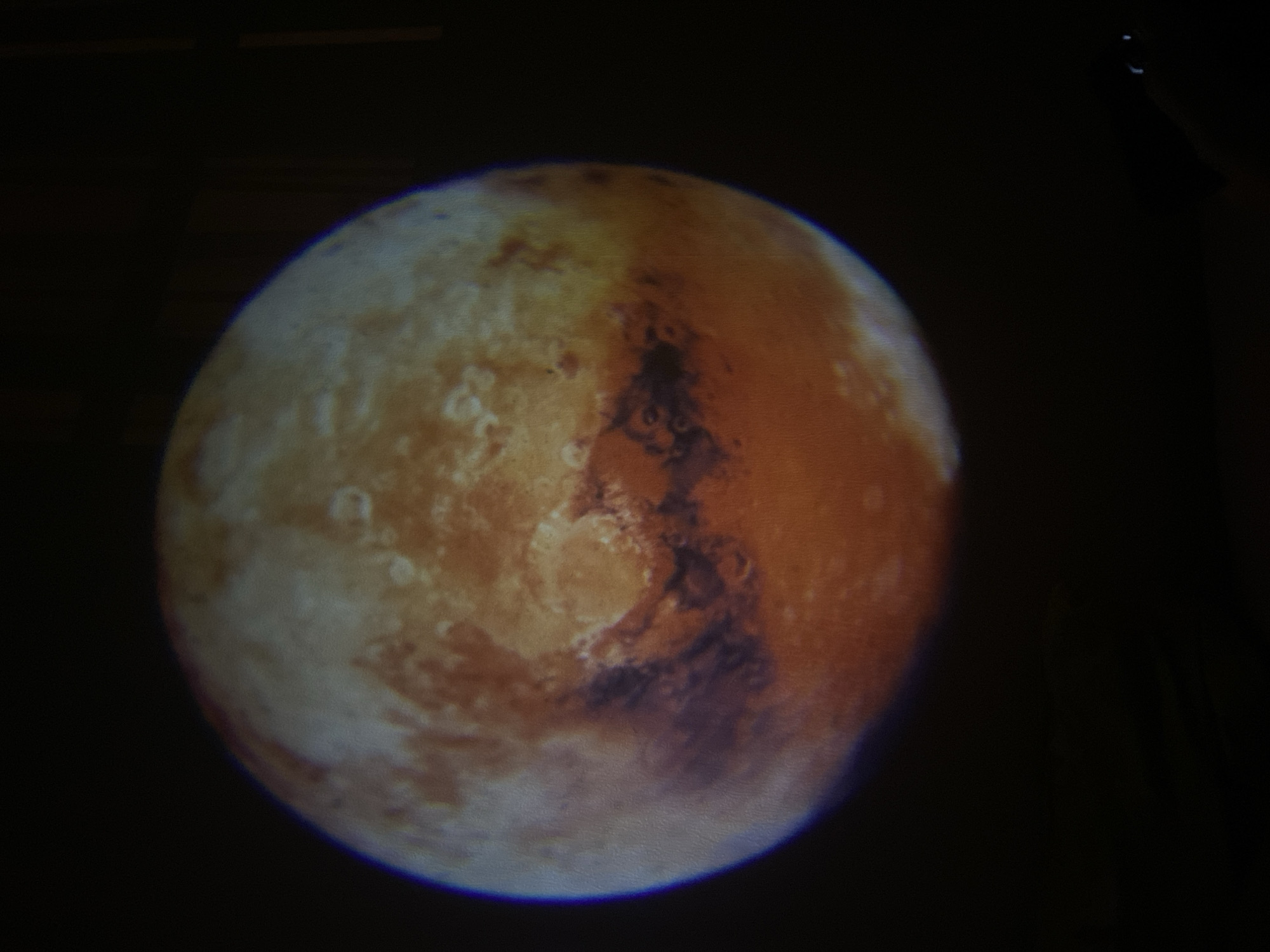 The image shows a spherical object resembling the planet Mars against a dark background. The object has a mottled surface with varying shades of brown, orange, and white. It is unclear if this is a photograph of the actual planet, a projection, or a model. There is no indication of the location being Saint Petersburg, Russia, or any information about people, actions, or interactions.