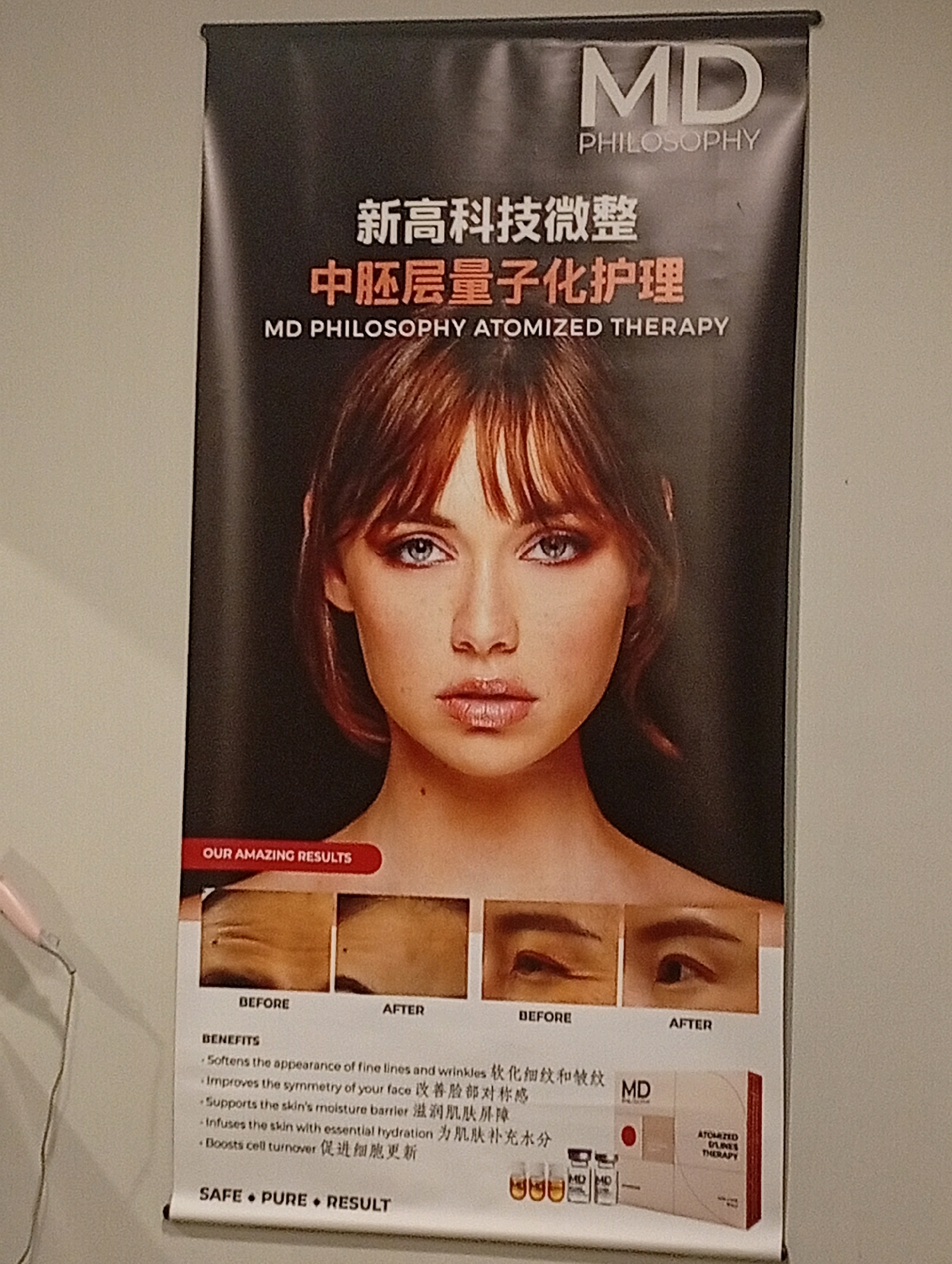 A vertical banner for "MD PHILOSOPHY ATOMIZED THERAPY" is displayed. The banner features a close-up of a woman's face, with her eyes and lips prominently displayed. Below the woman's face, there are two inset images showing before and after results of a facial treatment, focusing on the eye area. A list of benefits in English and Chinese is presented, followed by an image of the product packaging, which includes small bottles and a box. The phrase "OUR AMAZING RESULTS" is visible above the inset images, and "SAFE • PURE • RESULT" is at the bottom. The banner appears to be in an indoor commercial setting, possibly a beauty salon or a retail store, located within the Selayang Municipal Council, Malaysia.