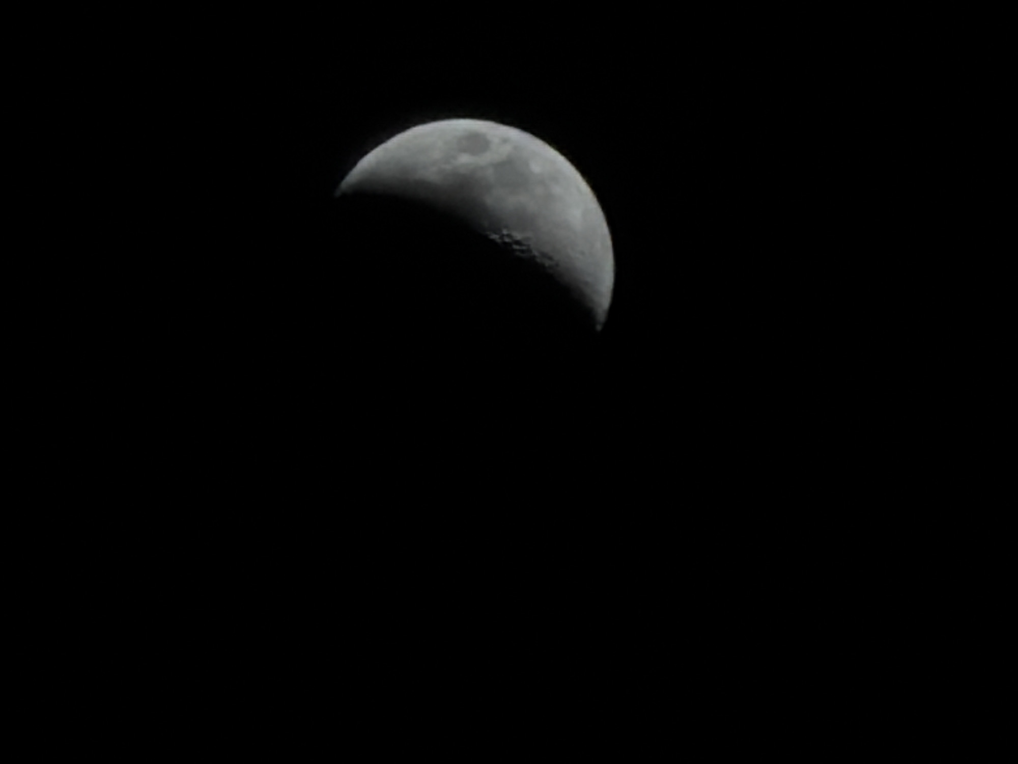The image shows a waxing crescent moon in a black sky. The location cannot be determined from the image alone. There are no people, subjects, objects, actions, or interactions visible in the image other than the moon itself and its environment.