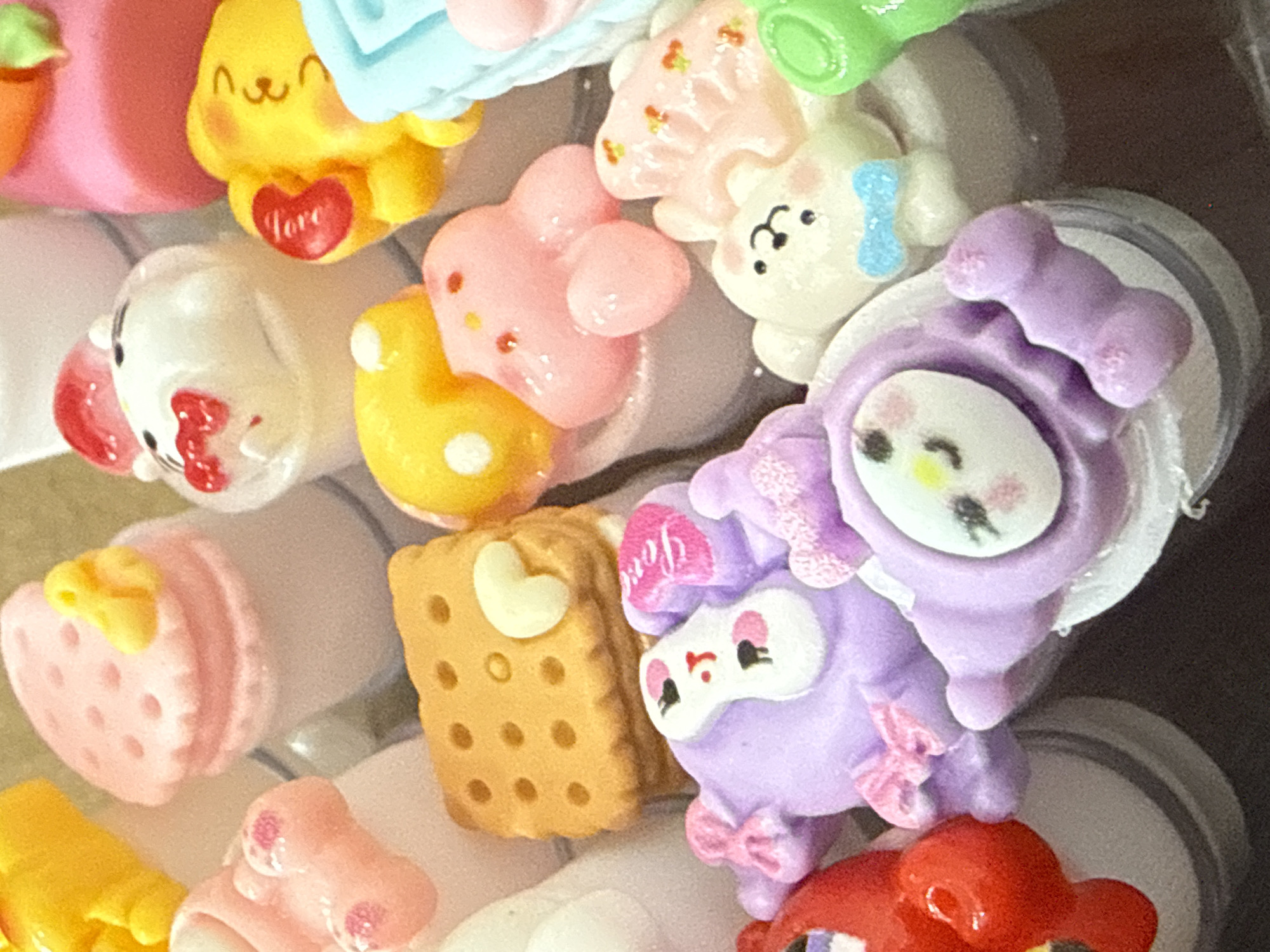 A close-up overhead shot reveals a cluster of colorful, cartoon-themed keycaps. A yellow keycap with a red heart is at the top left. To the right of it are white and pink keycaps, including a white one with a blue bow. A strawberry macaron keycap is at the bottom left. A tan keycap shaped like a cookie with a white heart is at the center. A lavender keycap of a cartoon character is at the right. It is not possible to verify if this image was taken in Chaikovsky, Russia, as there are no recognizable landmarks, people, or characteristics associated with that city or region.