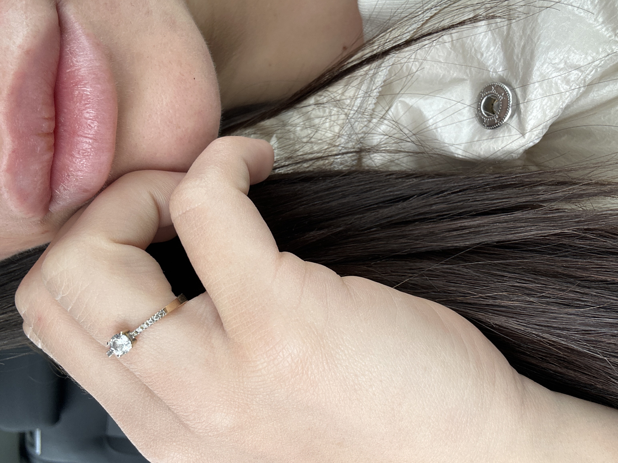 A close-up shot captures a woman lying down. Her face, specifically her lips, is prominently featured in the upper left. Her dark hair is spread out around her. The woman's hand is visible, adorned with a diamond ring. The setting includes a piece of white clothing with a silver snap fastener. The image provides no clues about whether the scene took place in the city of Plovdiv, Bulgaria.
