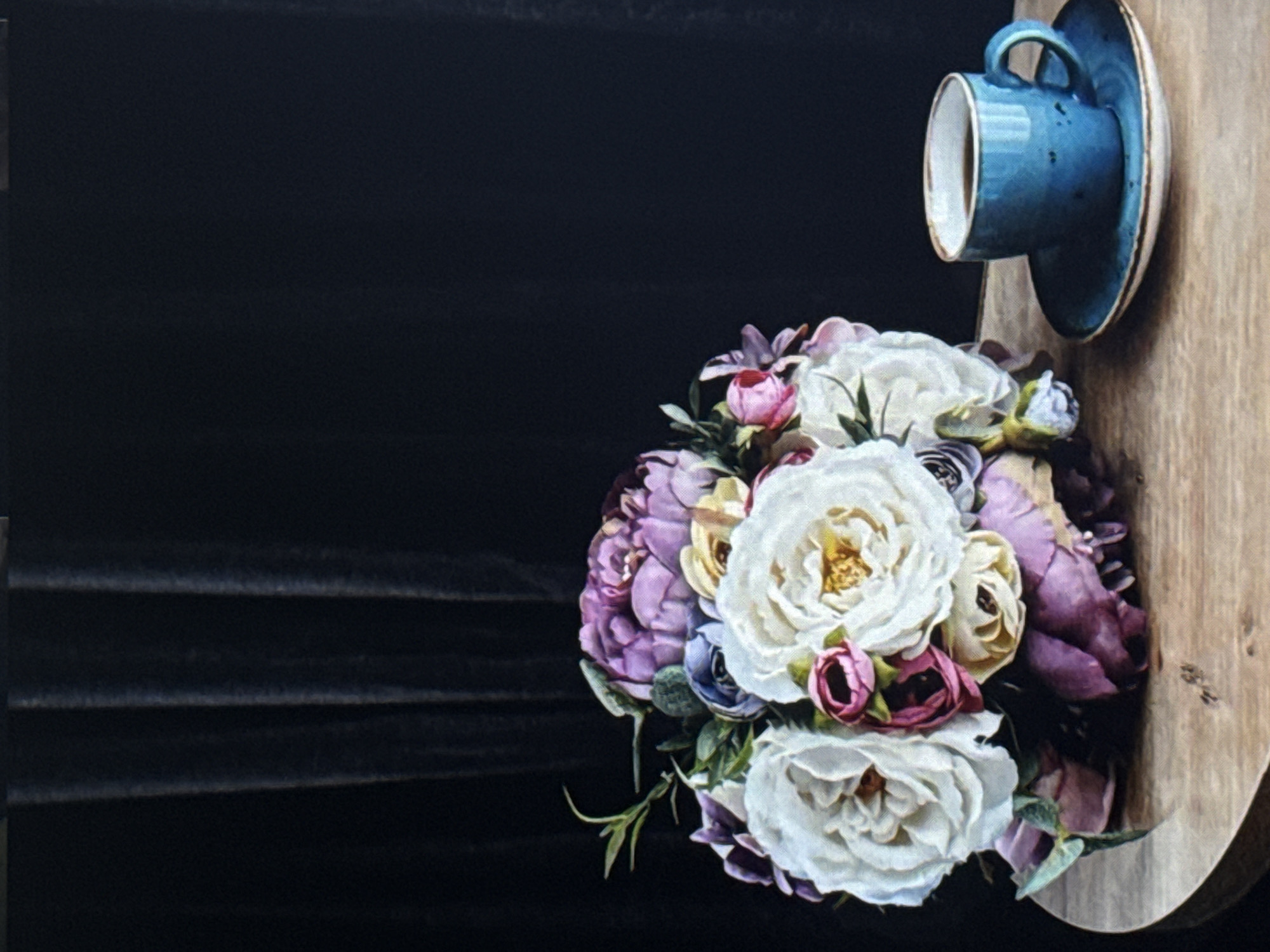 This media file depicts a close-up, artistic still life. The primary subjects are a bouquet of flowers and a blue ceramic teacup and saucer. The flowers are a mix of colors, including white, pink, purple, and yellow roses, arranged in a lush bouquet. The teacup and saucer are a vibrant blue, with a textured, speckled glaze, and are positioned on the right side of the frame, resting on a light-colored wooden surface. The background is a dark, textured material, possibly fabric or a dark wall, which creates a strong contrast with the subjects. The lighting appears to be soft, highlighting the details of the flowers and the glaze of the teacup. There is no text visible in the image. The overall mood is serene and elegant, evoking a sense of calm and beauty. The context of Eyüpsultan, Turkey, does not provide specific visual cues within the image itself, as the scene is a studio-like arrangement.
