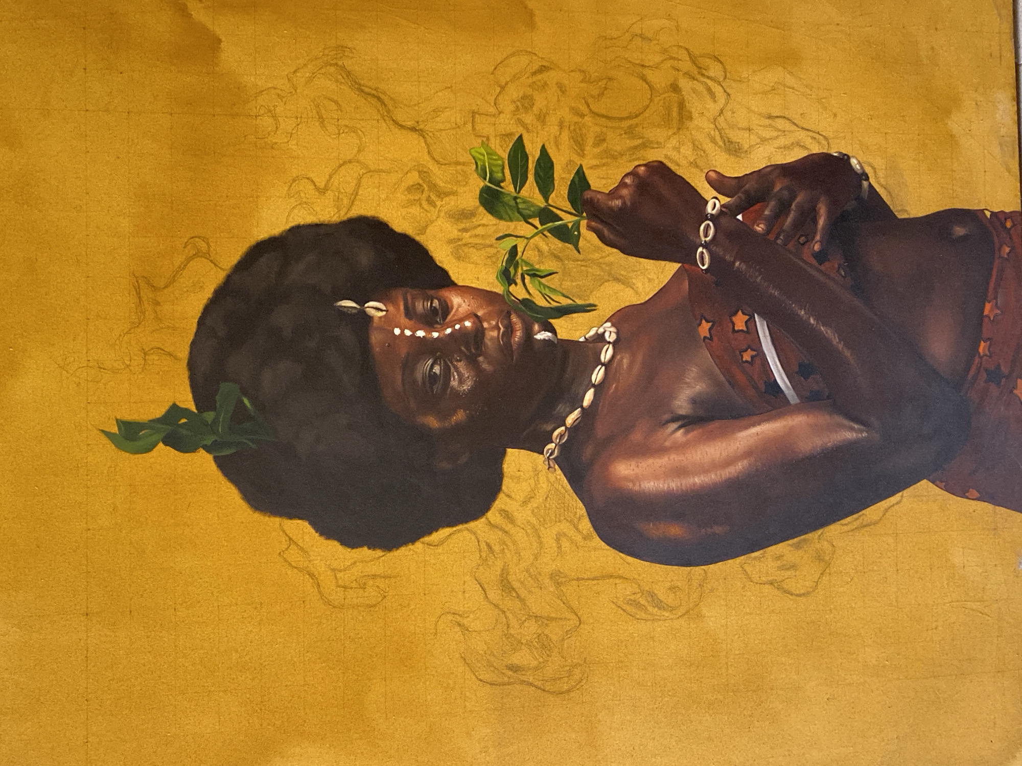A horizontal oil painting depicts a dark-skinned woman reclining against a gold background. She has dark, curly hair adorned with white cowrie shells along her hairline. Her skin is a deep brown with highlights suggesting a sheen of oil or moisture. She wears a necklace of cowrie shells and a red and orange garment with star-shaped patterns. Her left arm is bent across her chest, and her right hand holds a leafy green branch. The background is a uniform gold color with faint pencil sketches suggesting other figures or elements. This painting is located in Ado, Nigeria.
