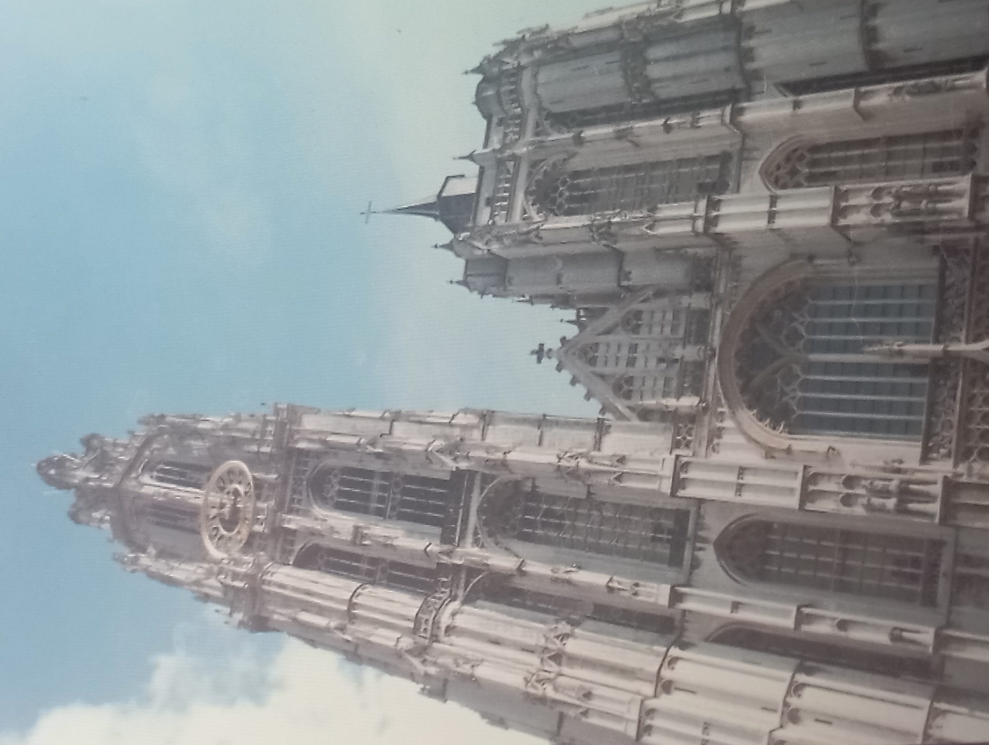 The image shows the Cathedral of Our Lady in Antwerp, Belgium. The cathedral is a large, Gothic-style structure with two towers. One tower features a clock. The sky is blue and there are some clouds visible. The photograph is taken from a low angle, looking up at the cathedral.
The location is not Karaganda, Kazakhstan.