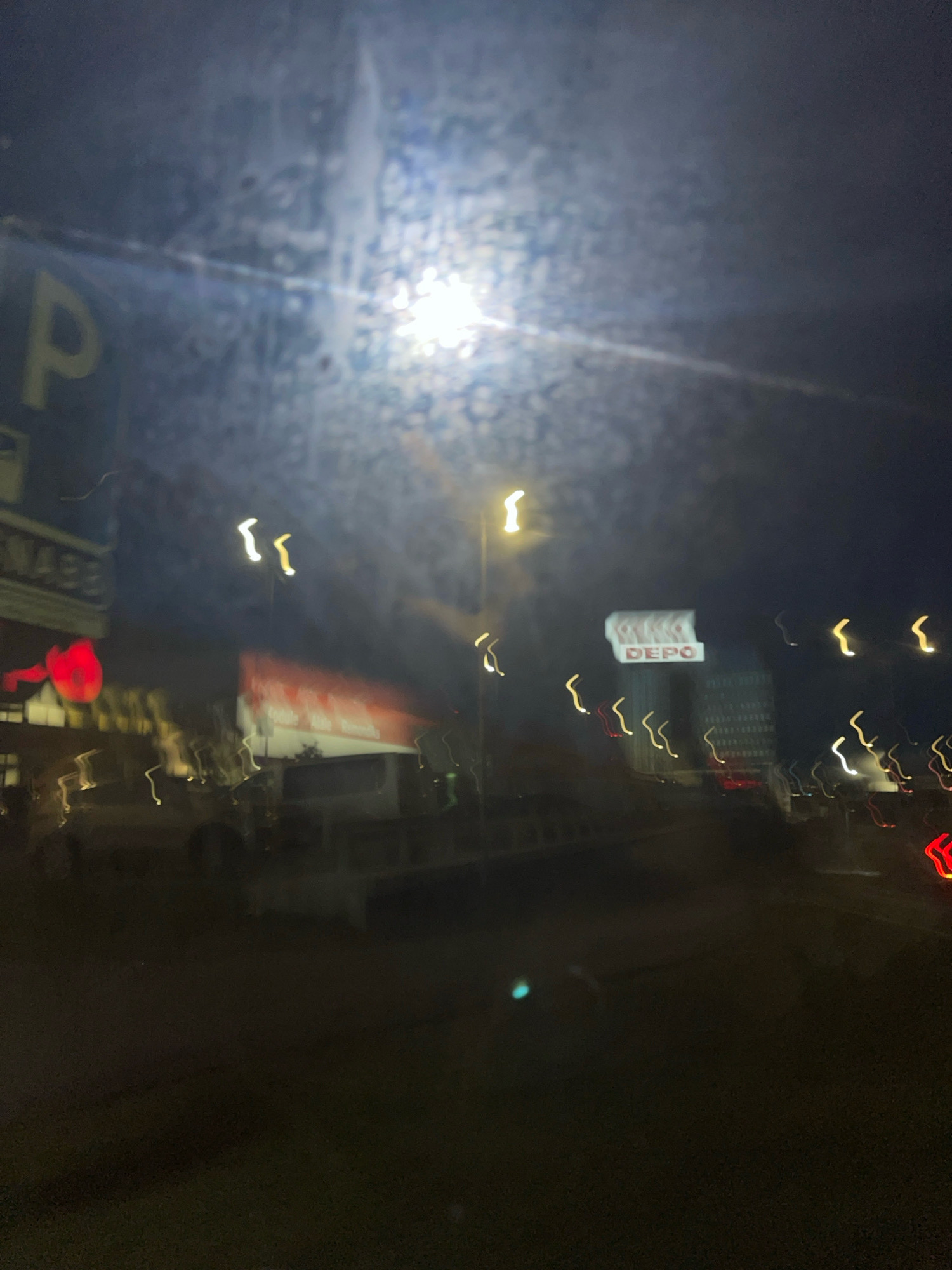 The image shows a blurry, nighttime scene of a street in Tallinn, Estonia. In the foreground, there is a blurry sign with the letter "P" on it. Further back, there are several blurry lights and signs, including one that appears to say "DEPO". There are also blurry shapes that suggest vehicles and buildings. The overall impression is of a dimly lit, urban environment, possibly taken from a moving vehicle.