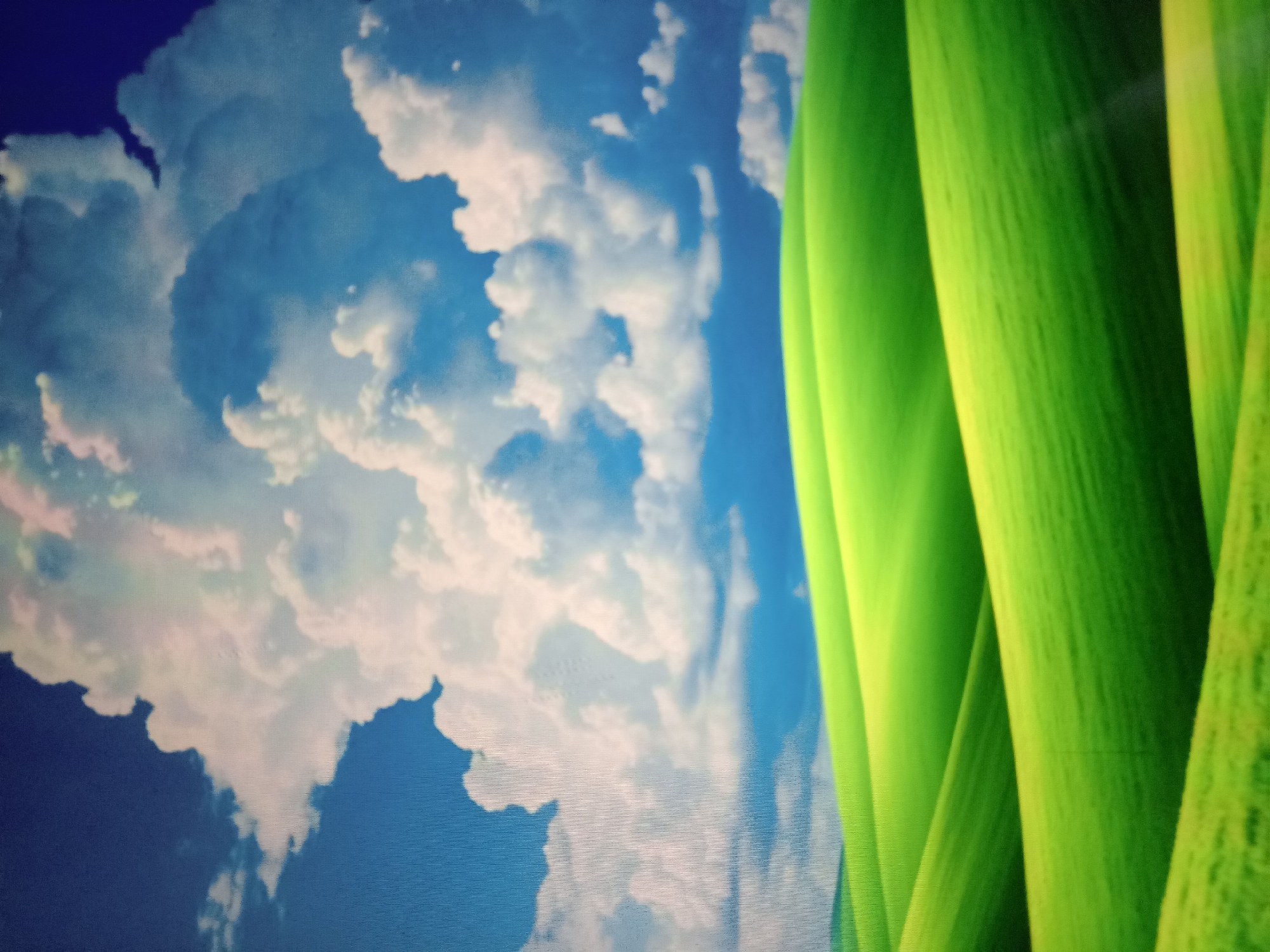 This is a digital image of a pastoral landscape, resembling the default wallpaper of Microsoft Windows XP. The scene features rolling green hills under a bright blue sky filled with fluffy white clouds. The perspective is low, emphasizing the gentle curves of the terrain. There are no people, structures, or any other discernible objects in the image. The image does not depict any specific location within Qorowul, Uzbekistan, or any other identifiable geographical area. It is a generic, idealized depiction of nature.