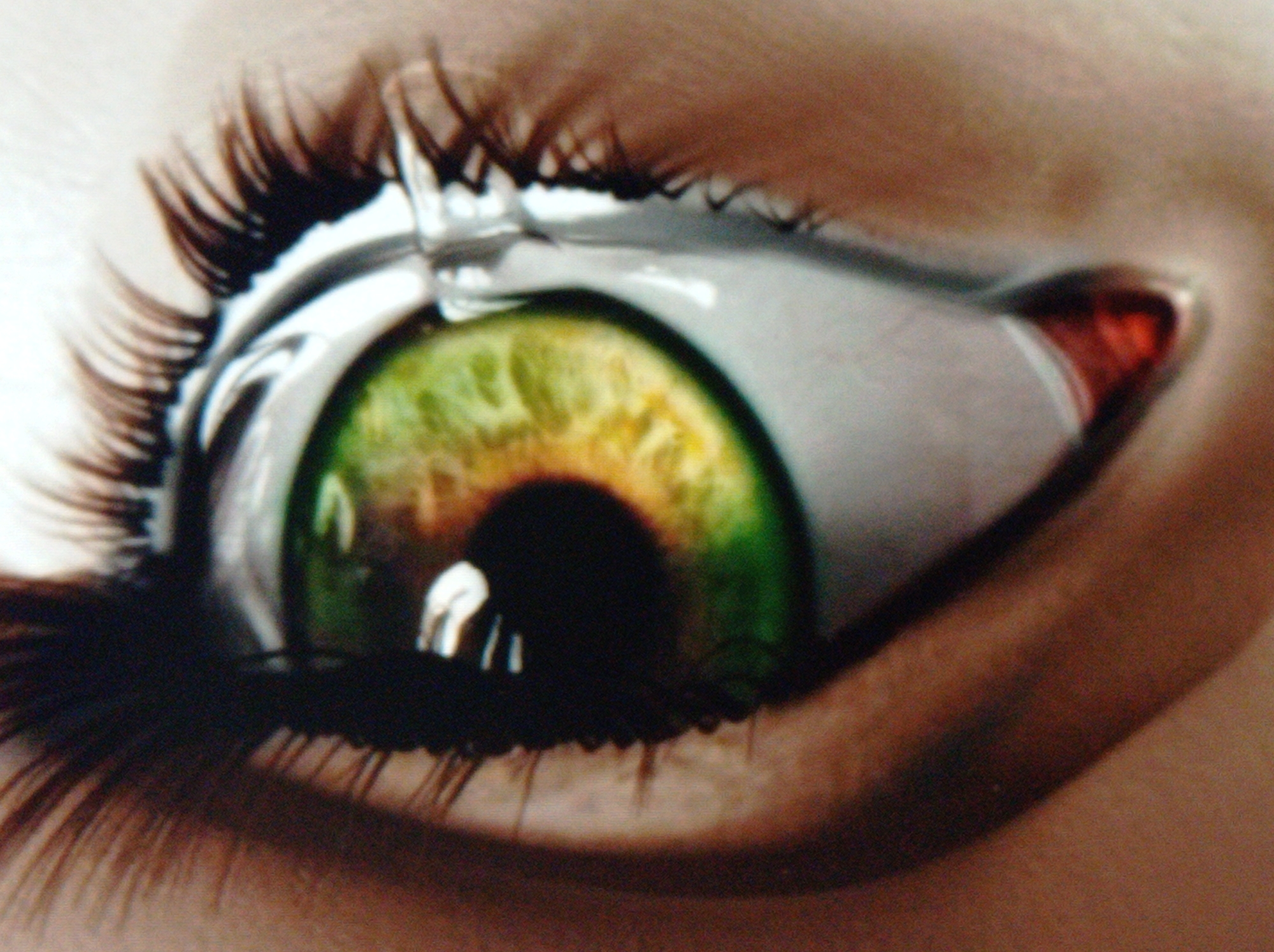 This is a close-up, high-angle, macro photograph of a human eye with a tear. The iris is a striking mix of green and yellow-orange, with a dark pupil. A single tear is visible, glistening and distorting the reflection on the lower eyelid. The eyelashes are dark and prominent. The surrounding skin is a warm, light brown tone. The image provides no information about the city of Mukachevo, Ukraine, or any urban environment. It focuses solely on the detail of the eye.