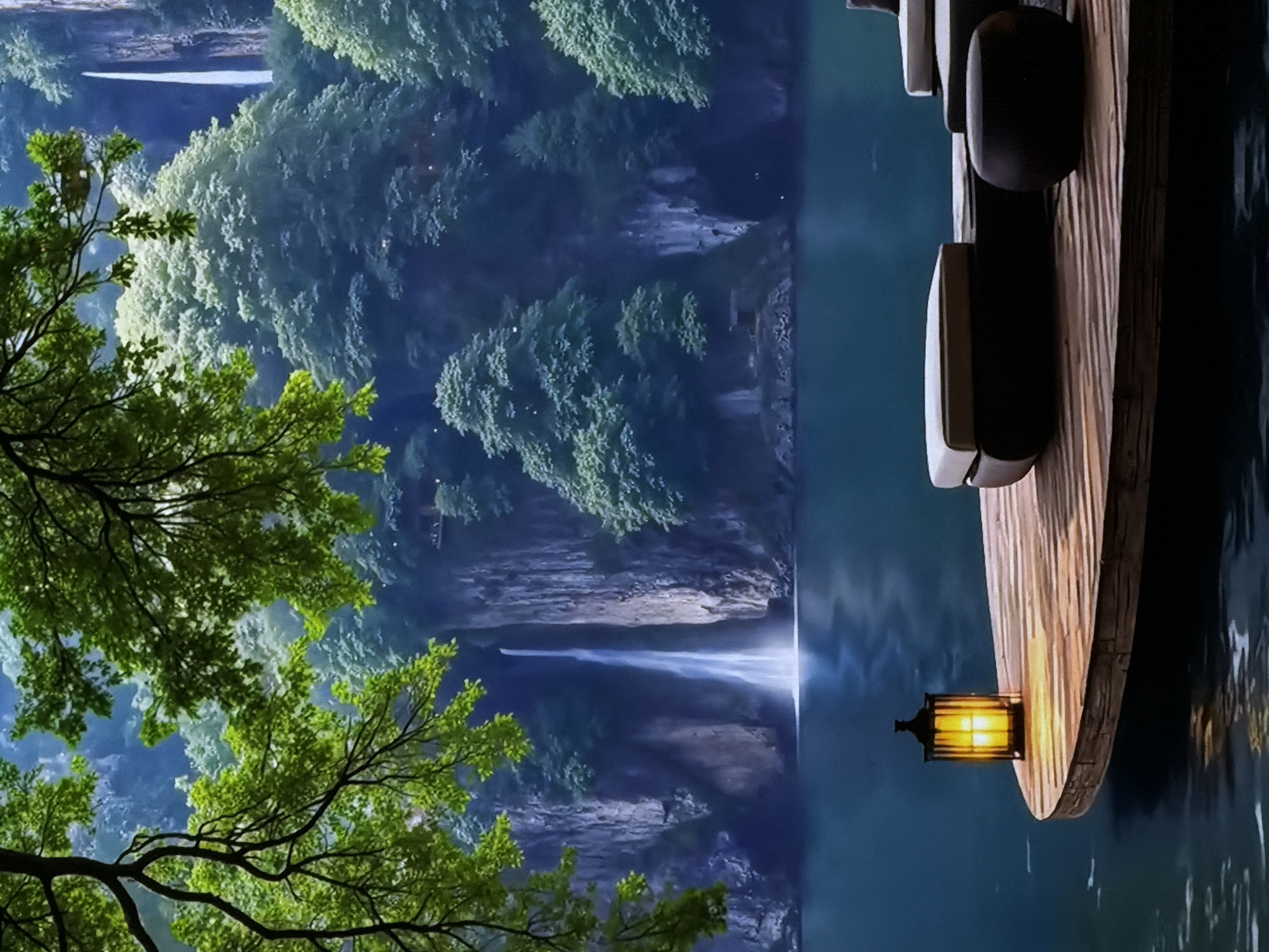 This digitally rendered image portrays a serene night-time landscape centered around a majestic waterfall. The scene is dominated by a large body of calm, dark blue water, likely a lake or river, stretching across the middle of the frame.
On the left side, vibrant green tree branches with dense foliage extend into the foreground, framing the view. Across the water, a powerful waterfall cascades down a tall, dark cliff face. The falling water emits a striking, bright luminescence, contrasting sharply with the deep blues and greens of the surrounding environment. The cliffs are adorned with lush, light green foliage that appears almost ethereal in the dim light.
To the right, a wooden structure, possibly part of a boat or a dock, is partially visible, extending into the water. A small, dark-metal lantern with warm yellow glowing panes hangs from this wooden platform, casting soft light on the wooden texture and creating a gentle reflection on the water's still surface.
The overall illumination suggests dusk or night, with the lantern and the glowing waterfall being the primary light sources. The atmosphere is one of profound tranquility and natural beauty. No individuals or specific activities are depicted. The artistic style lends a slightly stylized or fantastical quality to this natural setting. No text is visible in the image.