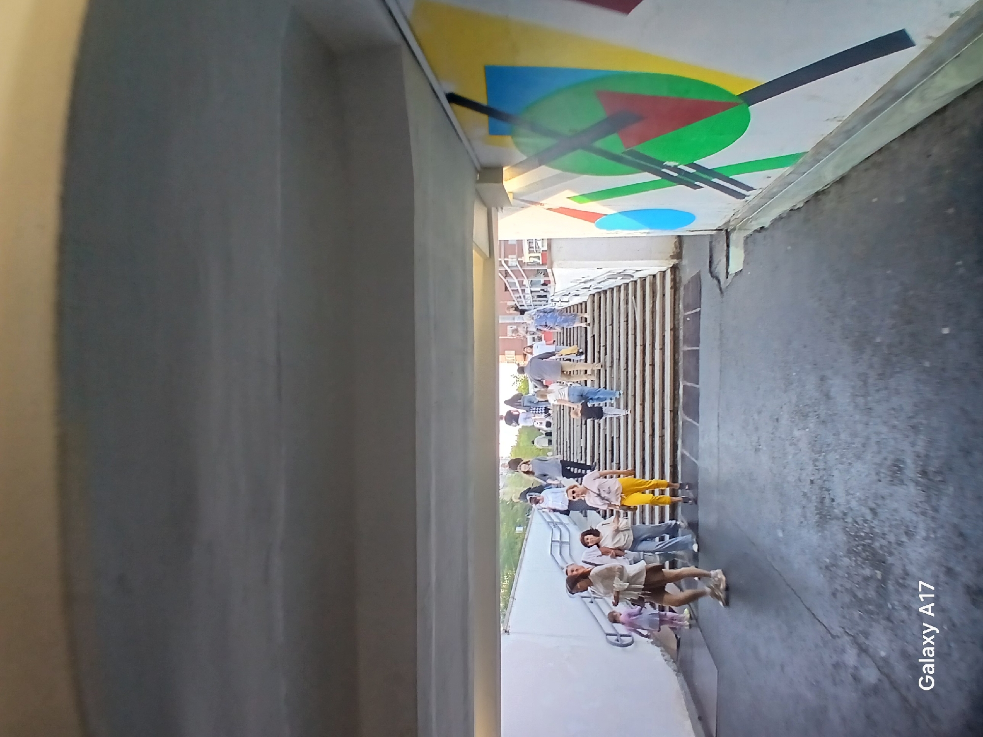 A long shot shows a group of people walking up steps in Yekaterinburg, Russia. Graffiti art is on the overhead concrete.
The camera phone information 'Galaxy A17' appears in the lower right.