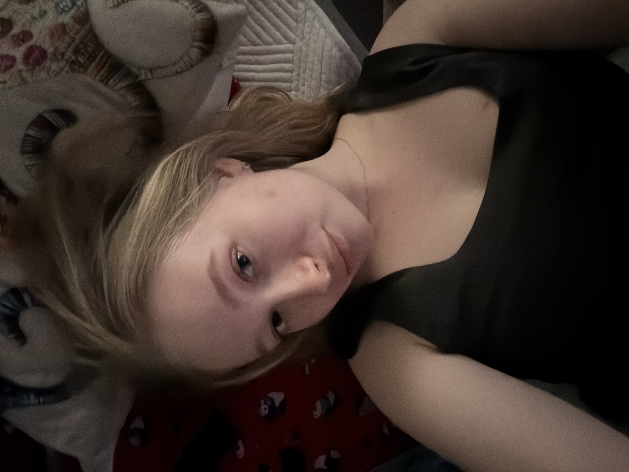 A fair-skinned female with blonde hair is lying on a bed. She is wearing a dark-colored shirt. The bed has a patchwork quilt and a red blanket with panda bear designs. The photo appears to have been taken indoors. The location is not evident from the image, thus its location in Penza, Russia, cannot be confirmed.