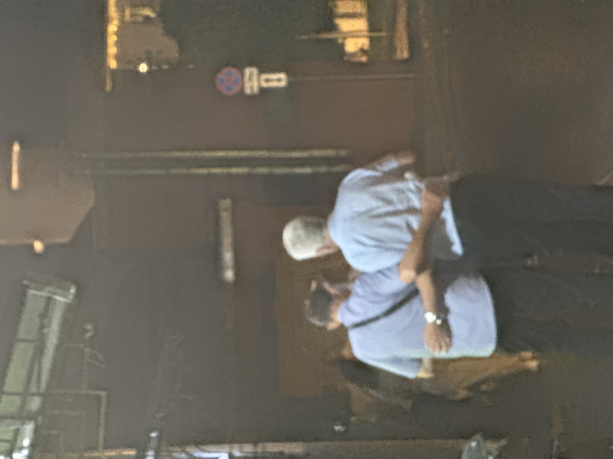 A low-resolution photograph captures two individuals on a street in what appears to be Moscow, Russia. One person, with gray hair, is wearing a light-colored shirt and dark trousers. The other individual, wearing a similar light-colored shirt and dark trousers, has their arm around the first person. A street sign is visible in the background.