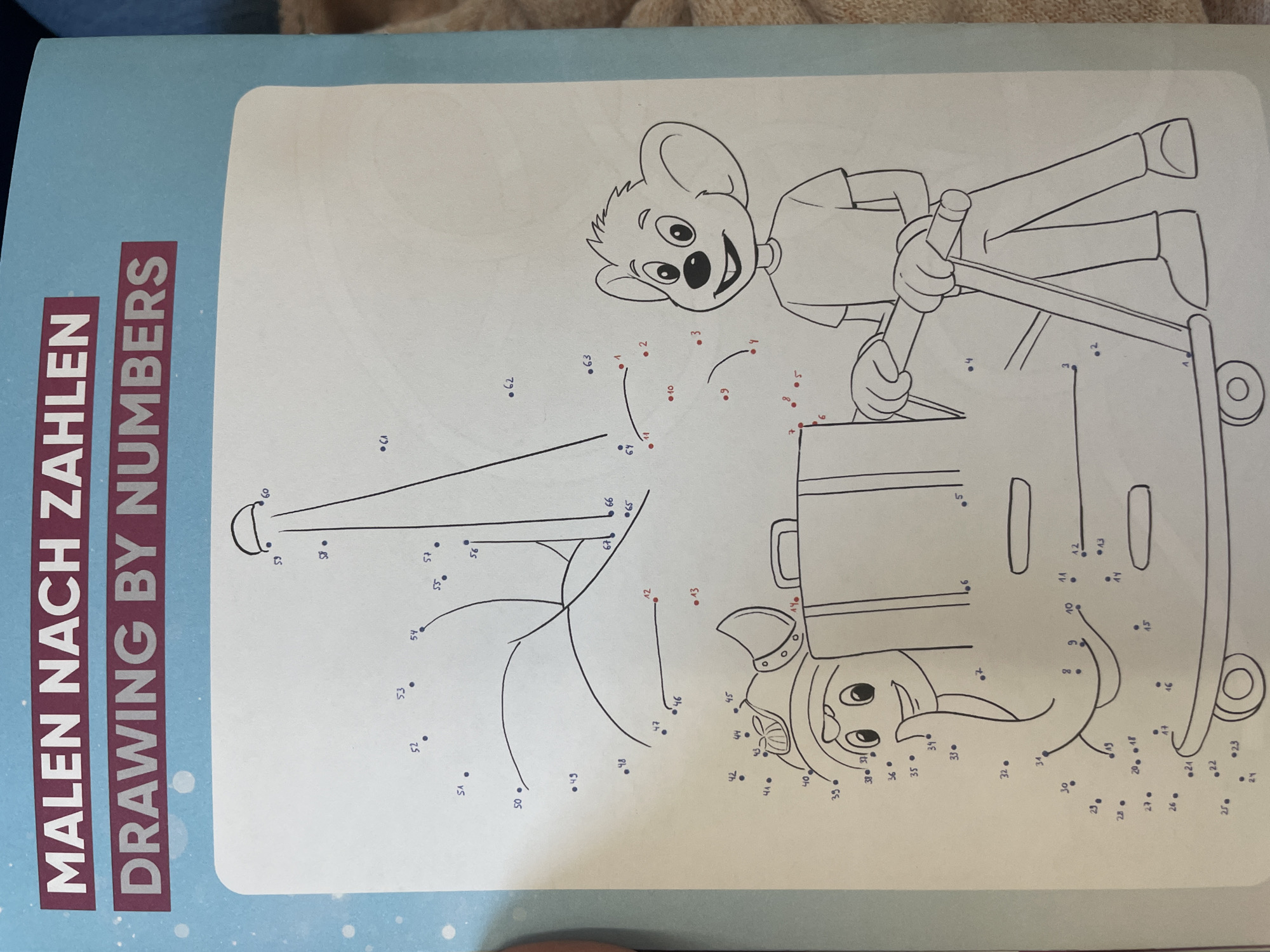 This is a close-up shot of a page from a children's coloring book. The page features a "Drawing by Numbers" activity with dots and numbers scattered across the page, intended to be connected to form an image. The visible portion of the image contains parts of a cartoon character, which appears to be a bear, holding onto a handle of a trolley or cart. Another character, possibly an elephant, is partially visible on the left side of the image. The background is a light blue with white snowflake-like patterns, suggesting a winter or festive theme. The title of the activity, "MALEN NACH ZAHLEN DRAWING BY NUMBERS," is prominently displayed in large, bold letters at the top of the page. The image does not contain any elements that would allow for the identification of a specific location in Hamburg, Germany.