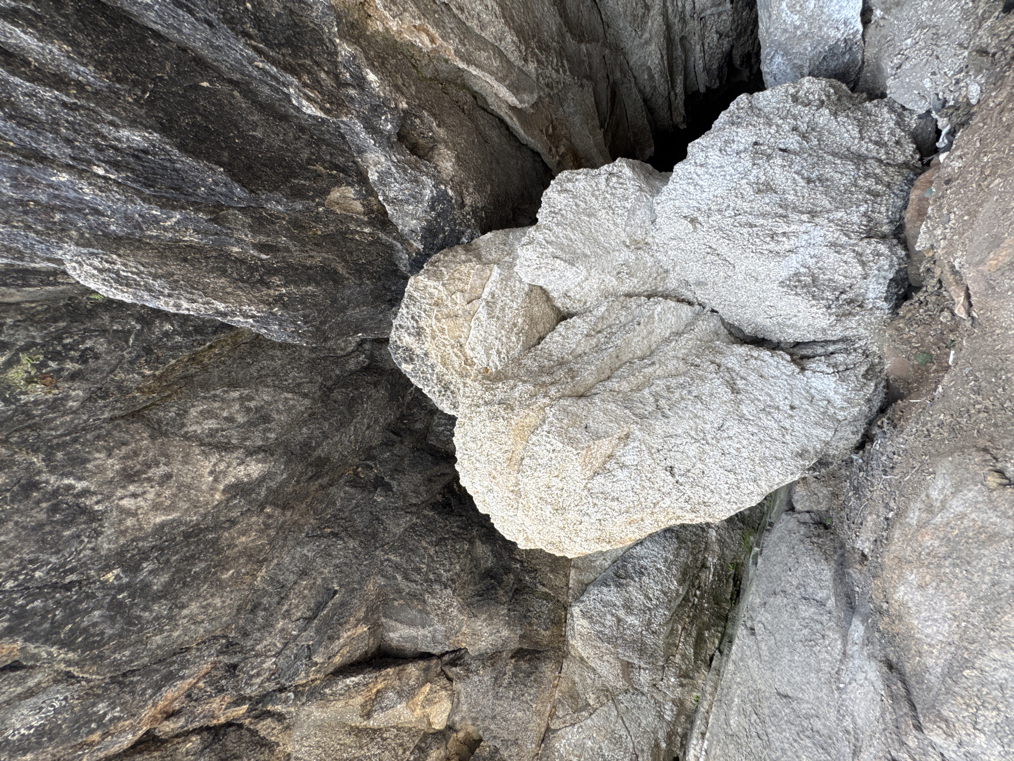 The image shows a natural rock formation in Dom Otdykha Zolotoy Plyazh, Russia. The formation is composed of large, rough-textured rocks. In the foreground, a cluster of pale, coarse-grained rocks is prominent. Behind these, darker, more layered rocks form a backdrop. The overall scene is outdoors, with visible elements of a rocky, natural landscape. There are no people or man-made objects visible in the image. The lighting suggests it is daytime.