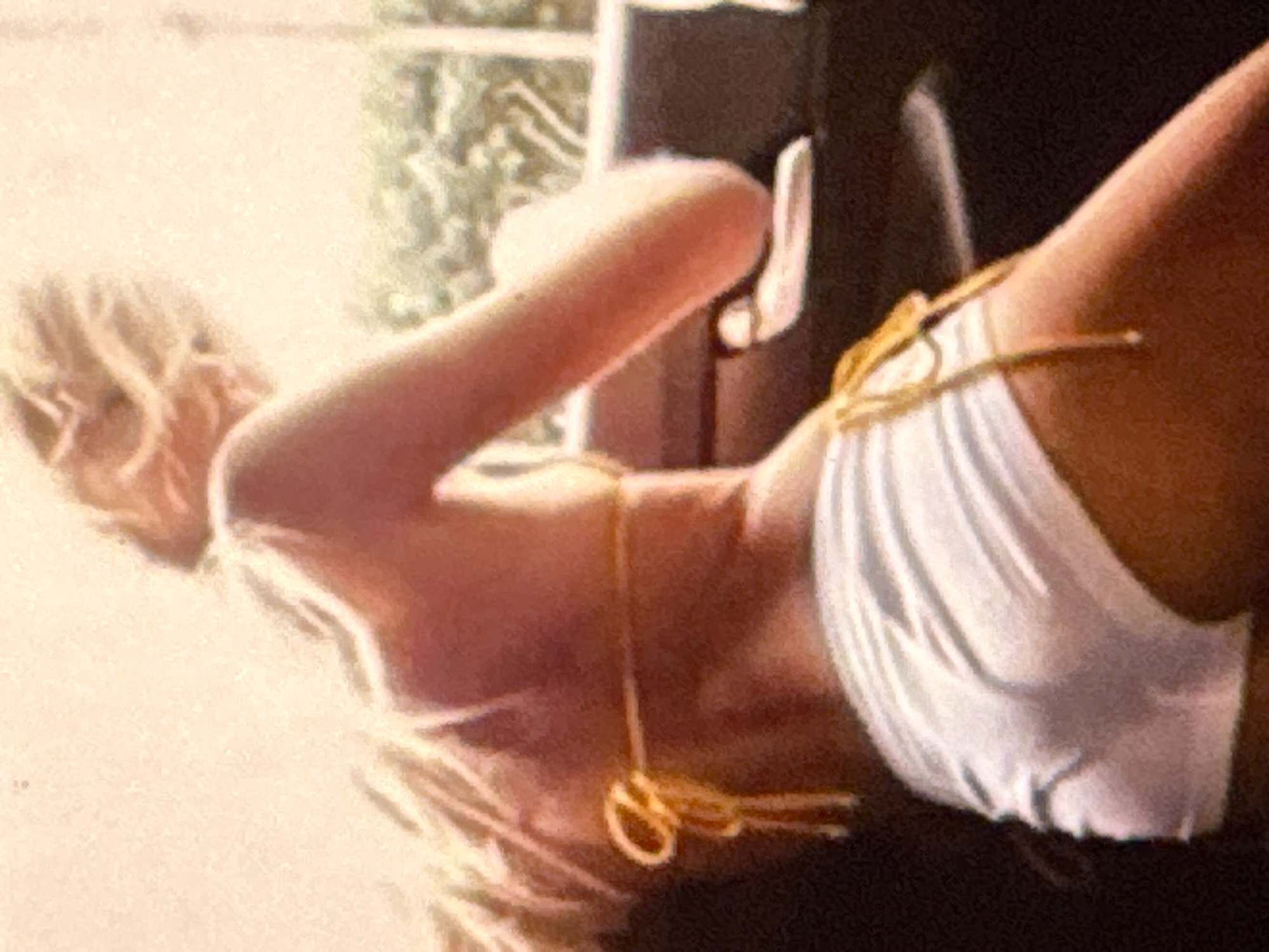 A person is seen from behind, wearing a white bikini bottom and a yellow bikini top. They are inside a vehicle, possibly a car, with a blurred background that suggests an outdoor environment, potentially with foliage. The person's back is turned to the camera, and their head is bent down, looking out of frame. The image appears to be taken during the daytime, with warm, natural lighting. The exact location in Kuta Selatan, Indonesia, cannot be determined from the provided image alone.