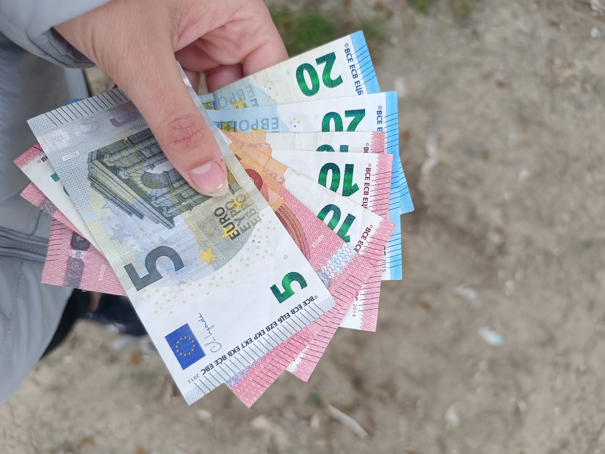 A person is holding several euro banknotes in their hand. The banknotes include a 5 euro note, a 10 euro note and a 20 euro note. The background is blurred. There is no information that the location is Pleven, Bulgaria.