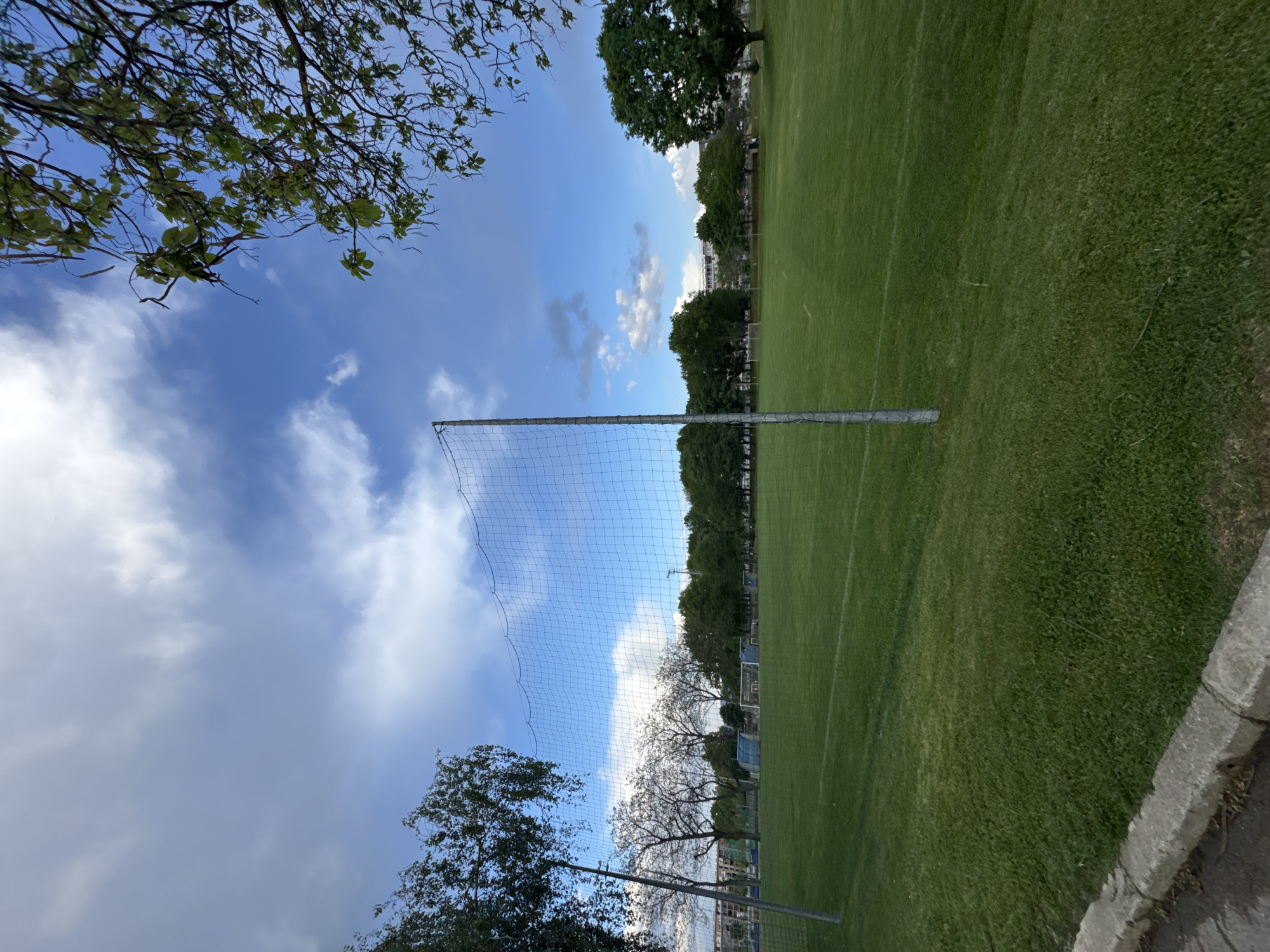 The image shows a soccer field in Sofia, Bulgaria, observed on a partly cloudy day. A soccer net is visible, and the field is surrounded by trees and a low concrete wall. No people are visible in the scene. The overall impression is that of a park or recreational area.
