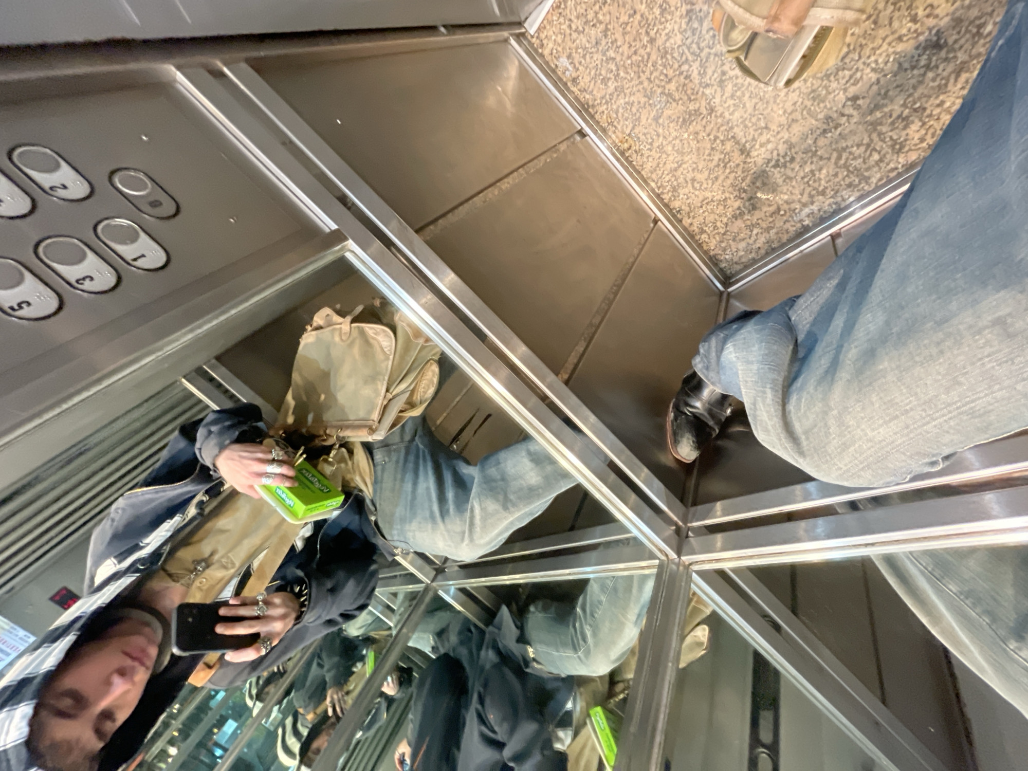 The image depicts a person taking a picture of themselves in a mirrored elevator. The elevator's control panel with buttons is visible. The elevator floor is also visible. The location is likely in Buenos Aires, Argentina, based on the request.