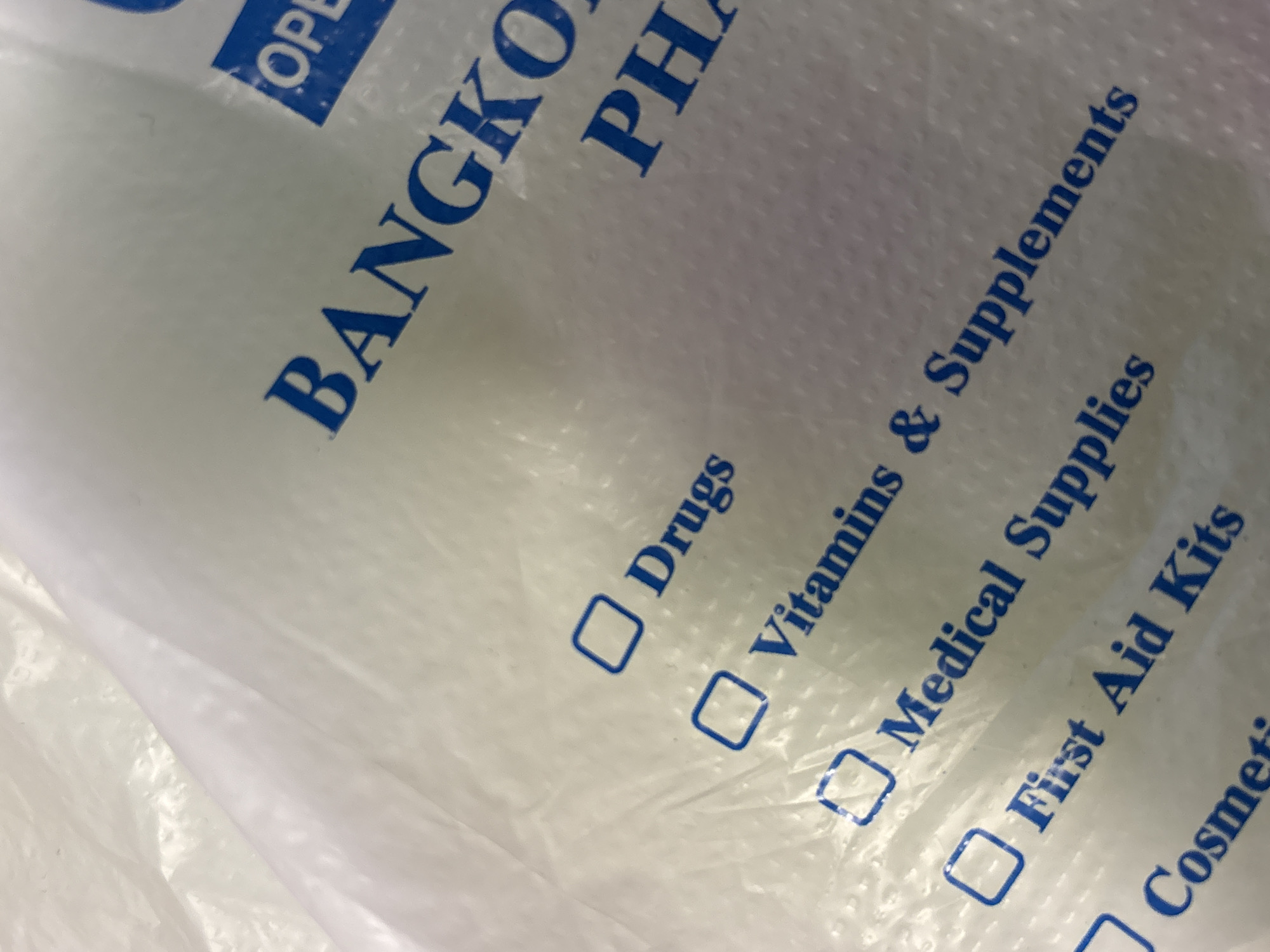 The image shows a close-up view of a printed plastic bag, likely from a pharmacy. "BANGKO PHA" is printed diagonally in large, blue, capital letters. Below that, are categories for items the pharmacy sells, each with a checkbox: "Drugs," "Vitamins & Supplements," "Medical Supplies," "First Aid Kits," and "Cosmetics." The checkboxes are empty. The plastic bag itself is crinkled and textured, with a white or light-colored background. The image gives no information regarding Perm, Russia.
