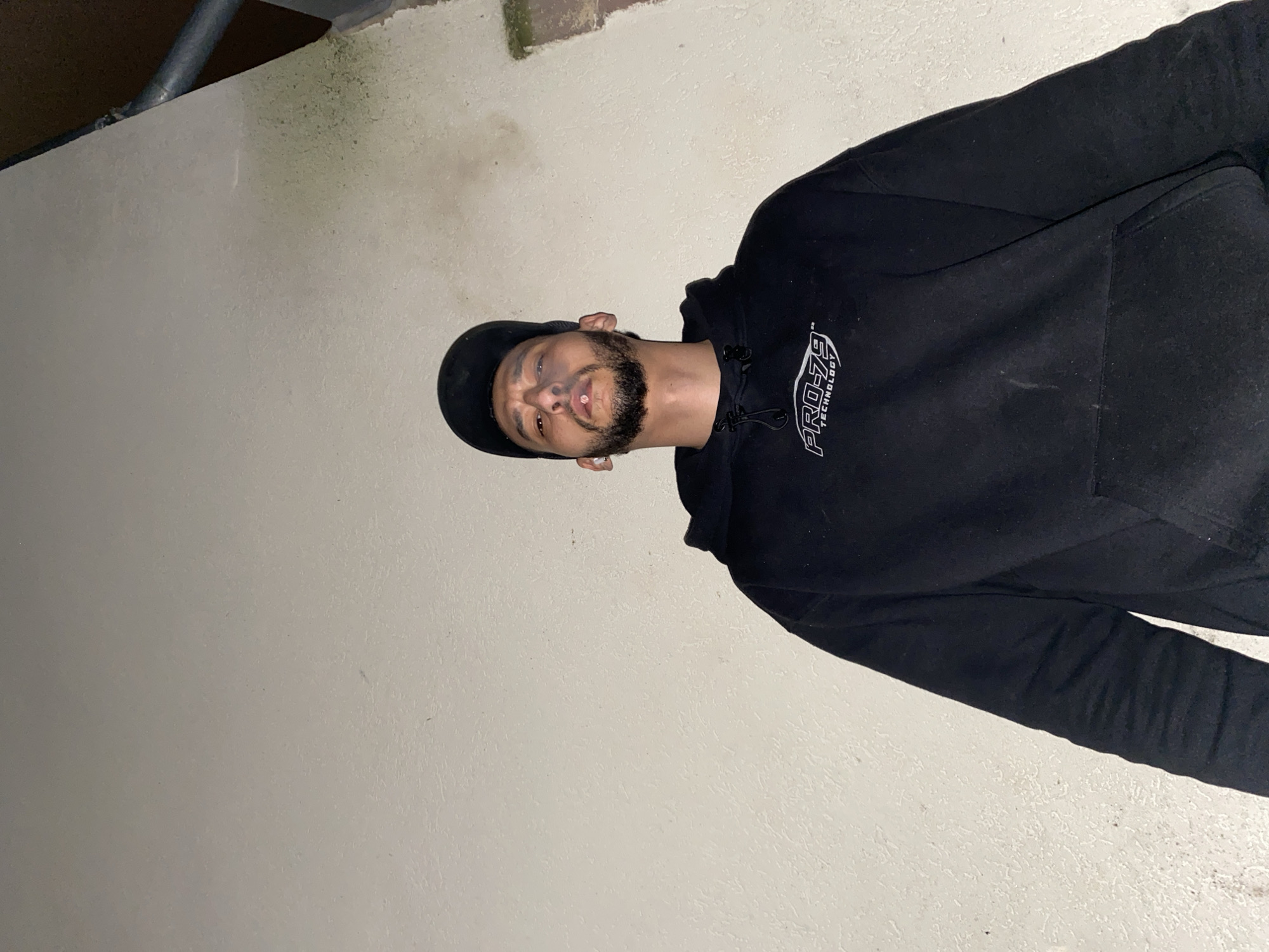 A man wearing a black baseball cap and a black hoodie stands against a white wall. He has a beard. He is looking at the camera. The word "PRO-79" is visible on his hoodie. The location appears to be indoors. There is no indication of the city of Schiltigheim, France.