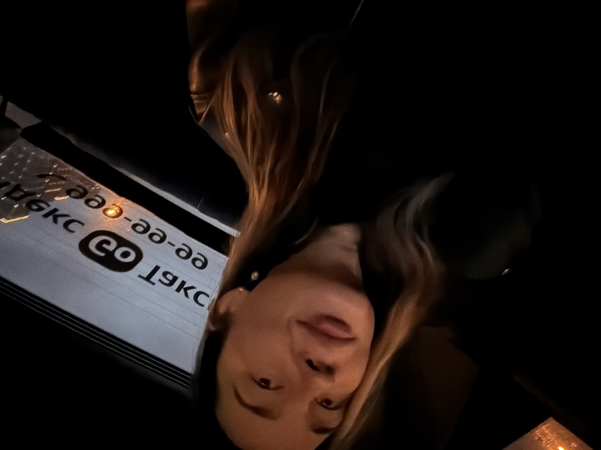 A woman is in a vehicle in Moscow, Russia. The reflection of a street sign with "Moscow" (in Russian) and the logo of "GO" is visible on the window. The image is dark.