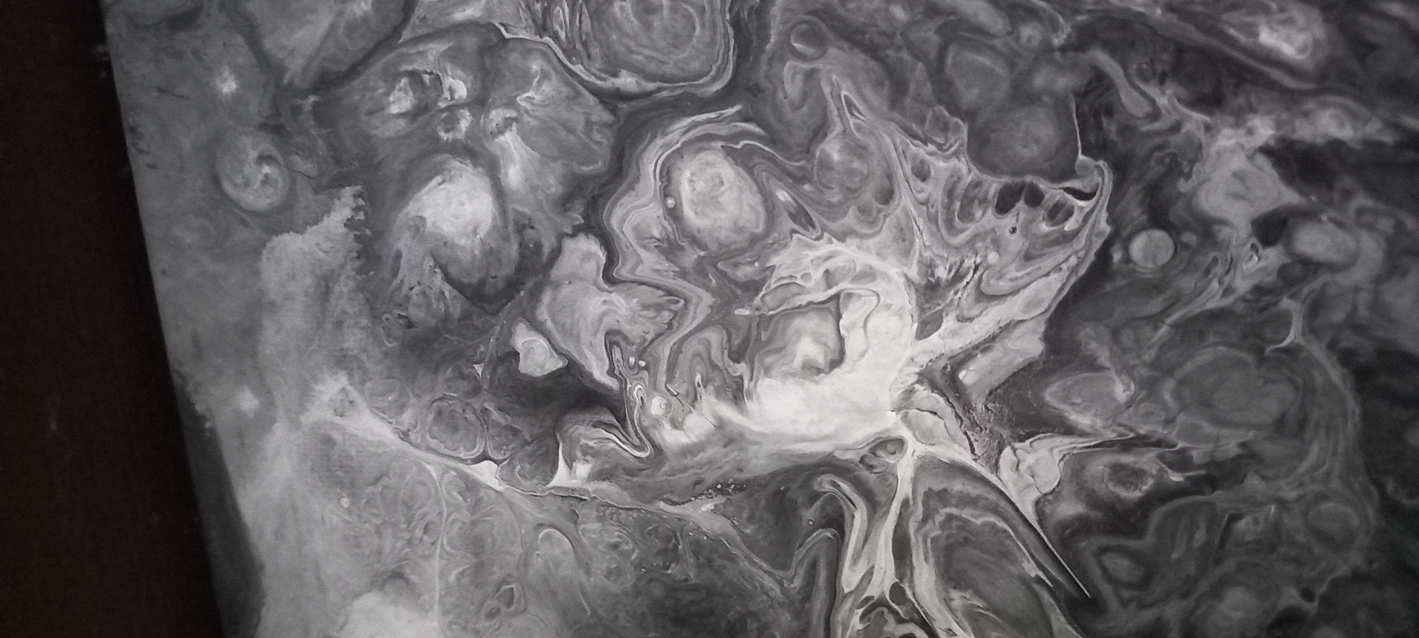 This is a grayscale abstract image with a marbling or fluid art effect. The swirling patterns of black, white, and gray create a sense of depth and movement. There are no discernible people, objects, or a specific scene. The image appears to be a close-up of a textured surface, possibly paint or a similar medium. The lighting creates strong contrasts, highlighting the fluid nature of the design. There is no visible text. The context of Kryvyi Rih, Ukraine, does not provide any visual cues within the image itself.