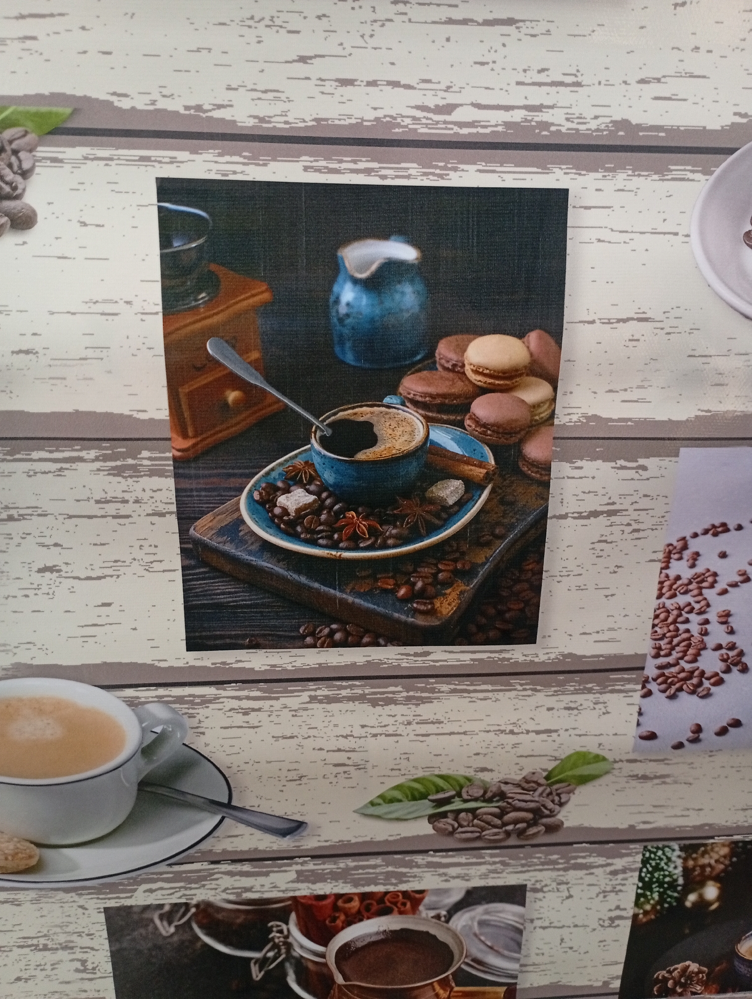 The image shows a collage of coffee-related imagery arranged on a wood-textured surface. One central image features a blue cup of coffee on a saucer, surrounded by coffee beans, star anise, a cinnamon stick, and a sugar cube. A vintage coffee grinder and a small blue pitcher are visible in the background of this central image. To the right of this, a close-up of scattered coffee beans on a light grey surface is displayed. Another image to the left shows a white cup of coffee with a spoon and a cookie. Below the central image, two more smaller images are visible: one shows jars with coffee or spices, and another features a pine cone and what appears to be a Christmas tree. The overall scene does not depict any specific location in the city of Borovichi, Russia, nor any people or actions.