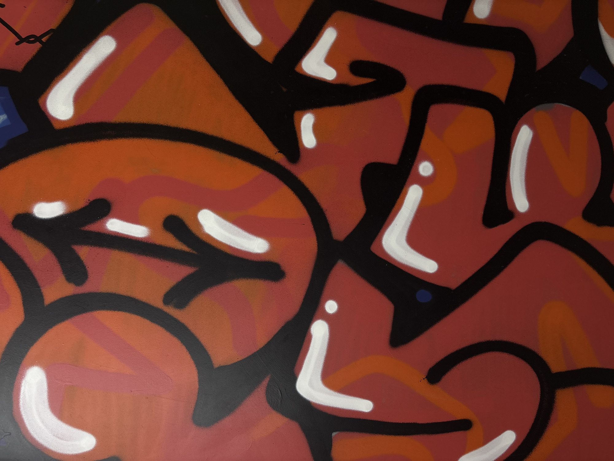 This media file displays a vibrant, abstract graffiti artwork, likely a close-up section of a larger mural. The primary subjects are bold, stylized shapes and forms characteristic of urban art.
The artwork features a dynamic interplay of colors, predominantly various shades of red and orange, outlined with thick, prominent black lines. White highlights are strategically placed on many of the colored shapes, creating a sense of depth and giving them a glossy, three-dimensional appearance, as if catching light. Small accents of blue are also visible in a few spots, adding contrast.
The style suggests heavily stylized lettering, although no discernible words or coherent text are clearly visible. Instead, the forms are intricate and interconnected, with rounded edges, sharp angles, and flowing curves. On the left side of the main image, a distinctive arrow-like shape is incorporated into the design, pointing towards the right. The paint application suggests spray paint, with a somewhat uniform yet slightly textured finish.
No people, specific objects beyond the abstract art, or events are depicted. The focus is entirely on the intricate details and vibrant aesthetic of the graffiti itself. There are no visible cues regarding the time of day, weather, or specific location within Perm, Russia, other than the art itself suggesting an urban environment. The overall impression is one of energetic and complex street art.