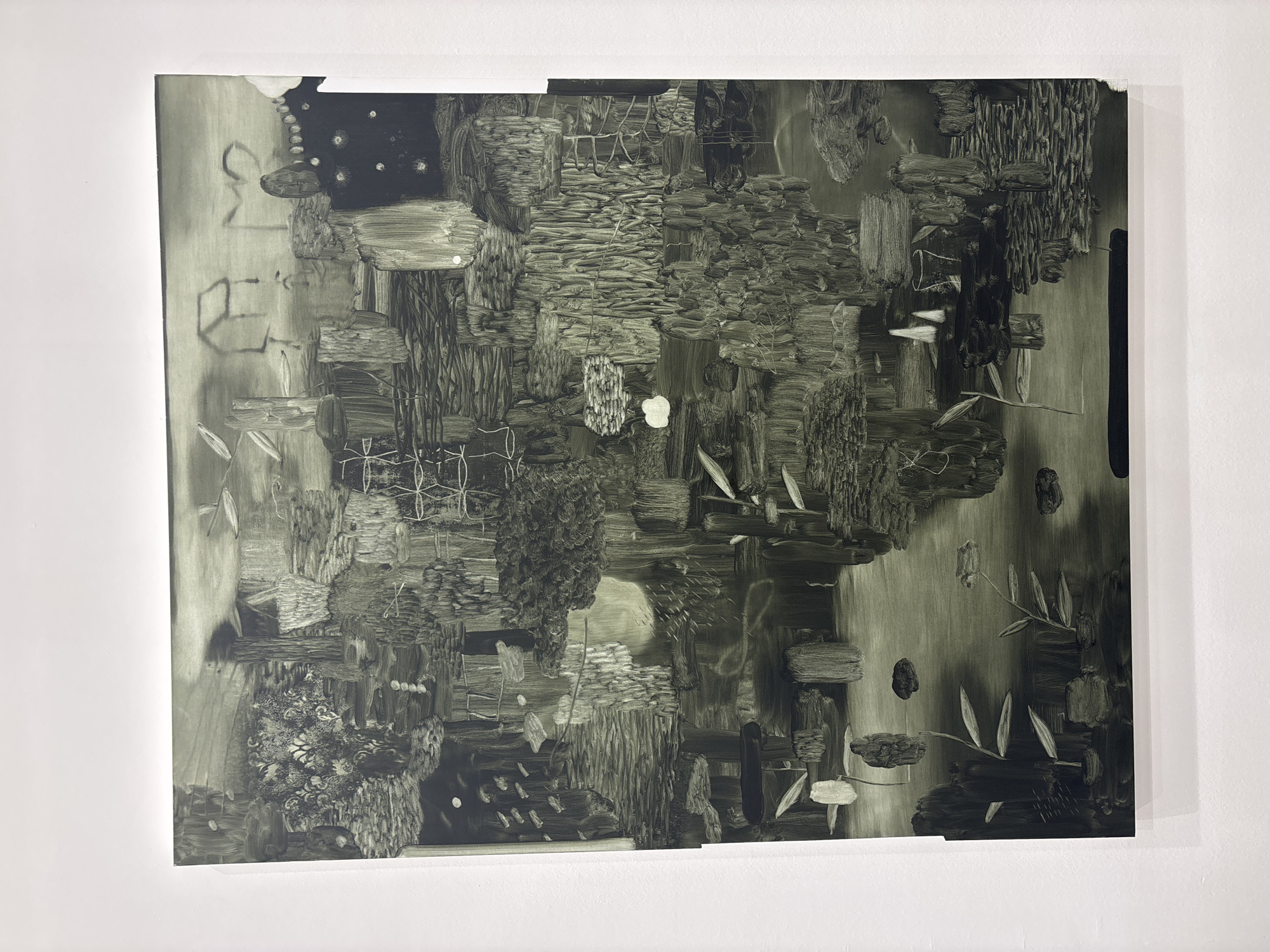 An abstract painting hangs on a white wall, likely in a gallery setting. The painting is predominantly in shades of grey, with a texture suggesting broad brushstrokes. The composition lacks clear representational elements, instead consisting of clusters of dark and light forms arranged in a fragmented manner. At the top left corner, there is a darker area with white dots. The top edge shows a small missing piece. The painting's surface reflects ambient light. The wall behind the painting is plain and white. The painting is of unknown provenance and style. It is not possible to ascertain the location in Milan, Italy.