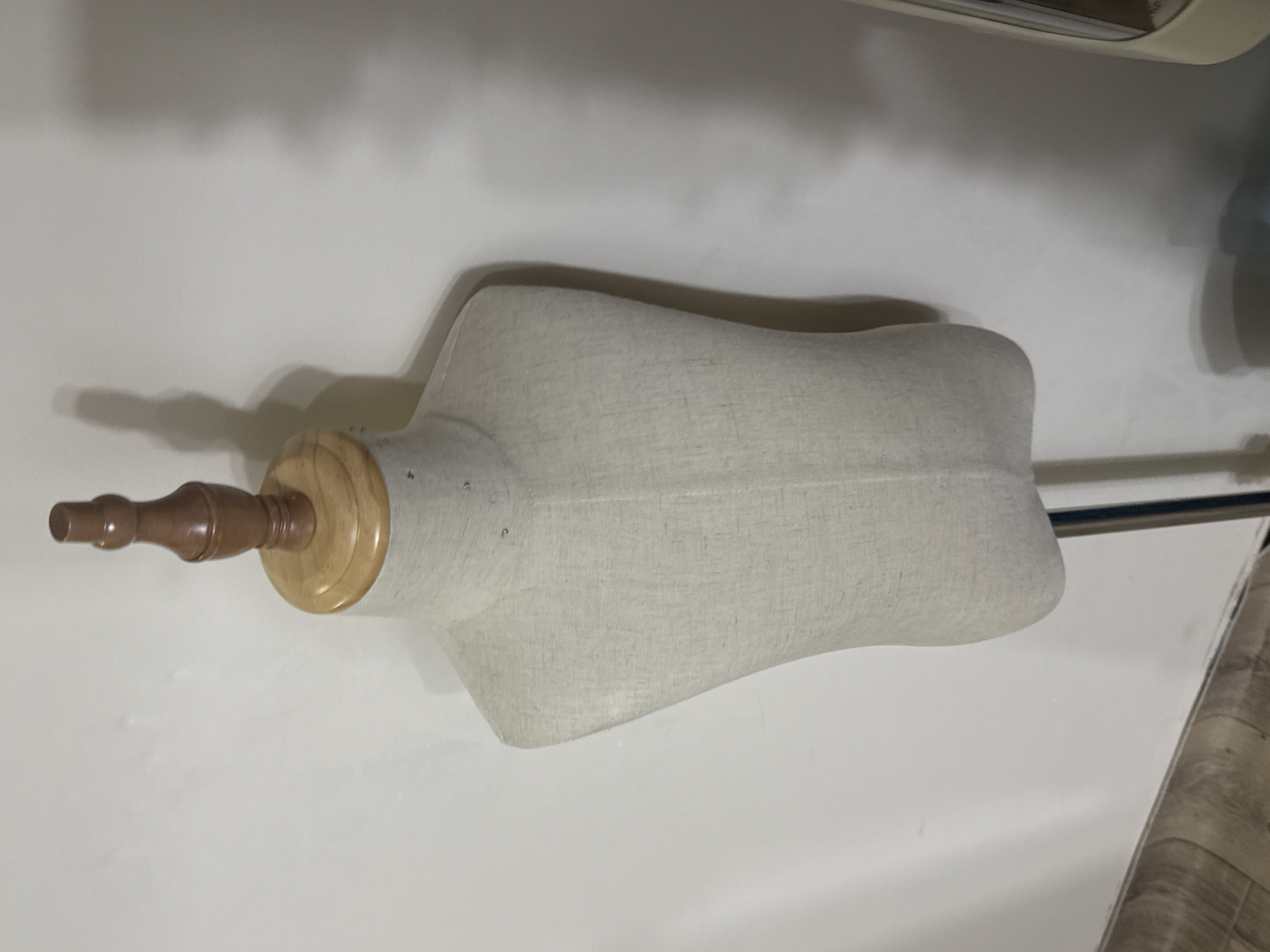 The image shows a partially visible tailor's dummy against a plain white background. The dummy has a brown wooden neck and a light-colored fabric-covered torso. A metal rod extends from the side of the torso. The dummy is in a horizontal position, as if lying on its side. The image contains no information that would allow one to infer a location in Yerevan, Armenia, or any other geographic location.