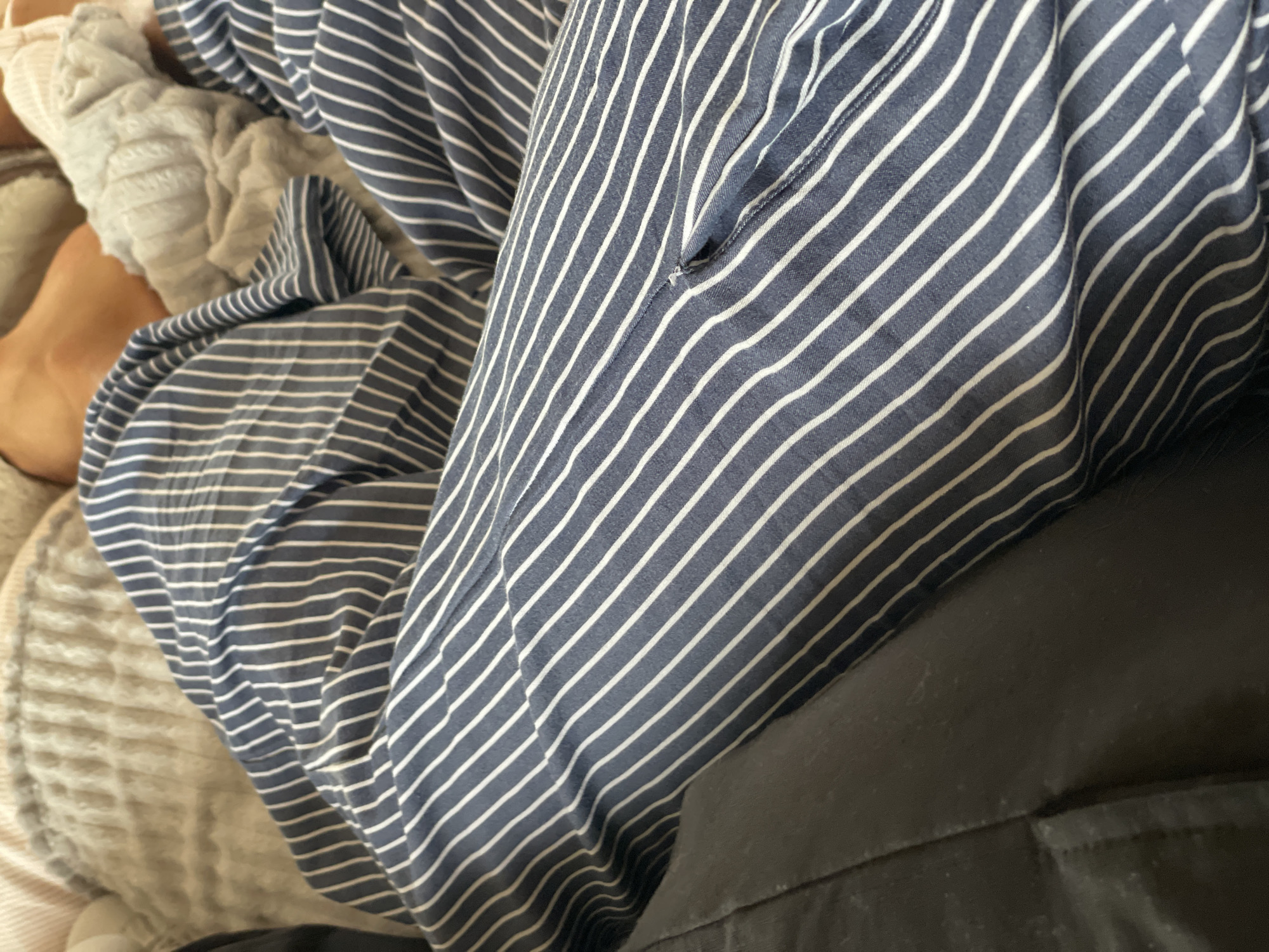 The image presents a close-up shot of various textures and patterns. Predominantly, there is a striped fabric, blue with white lines, possibly a piece of clothing or bedding. The fabric seems to be draped or folded, obscuring the object it covers. To the right, a dark, solid-colored material, likely fabric, is visible. On the left, a soft, textured surface appears, potentially a blanket or upholstery with a creamy-beige tone. The scene lacks any identifying features to link it to Sestroretsk, Russia. There are no observable people, actions, or interactions.